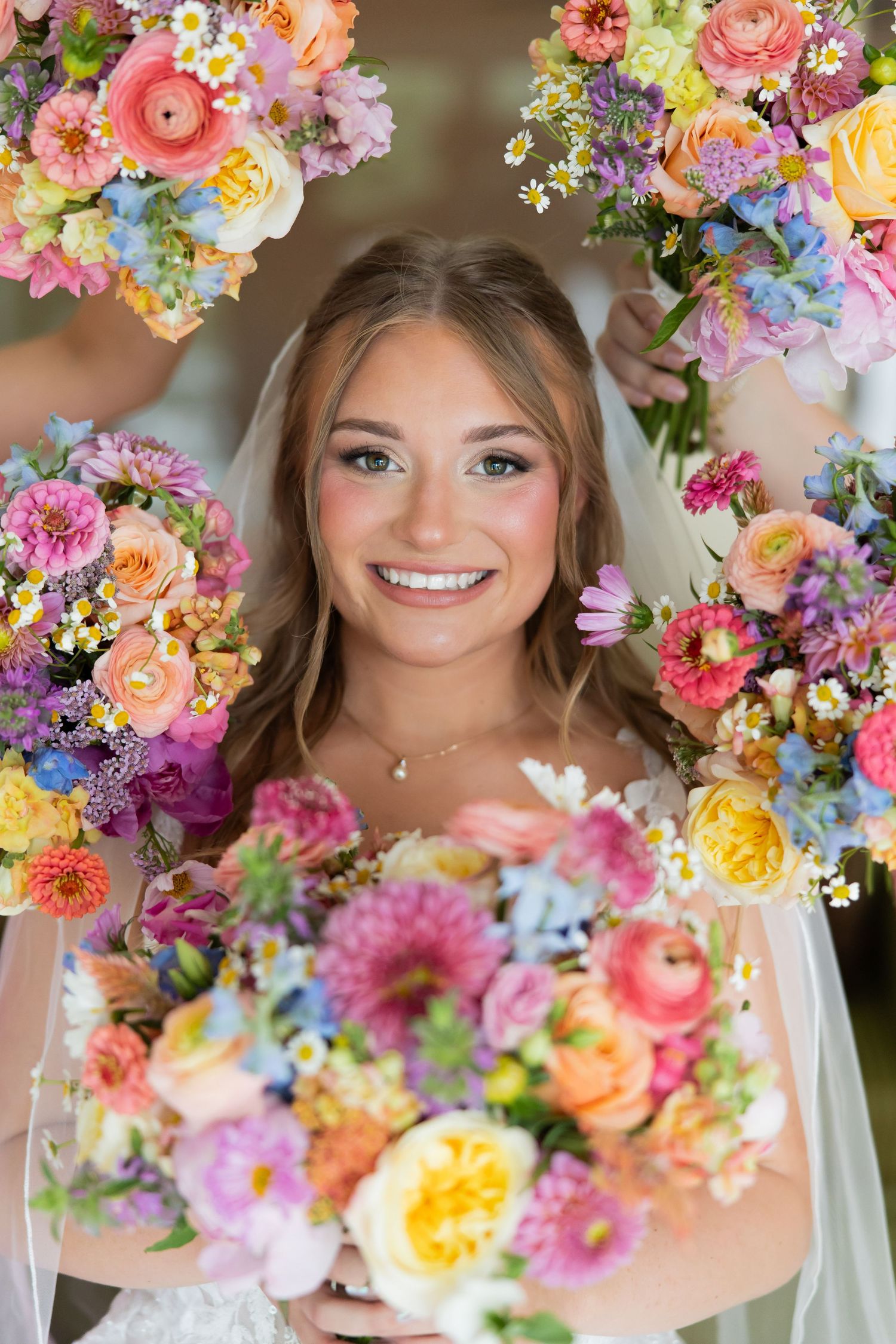 Smiling bride surrounded by colorful bridesmaids bouquets featuring pink, yellow, and orange blooms.