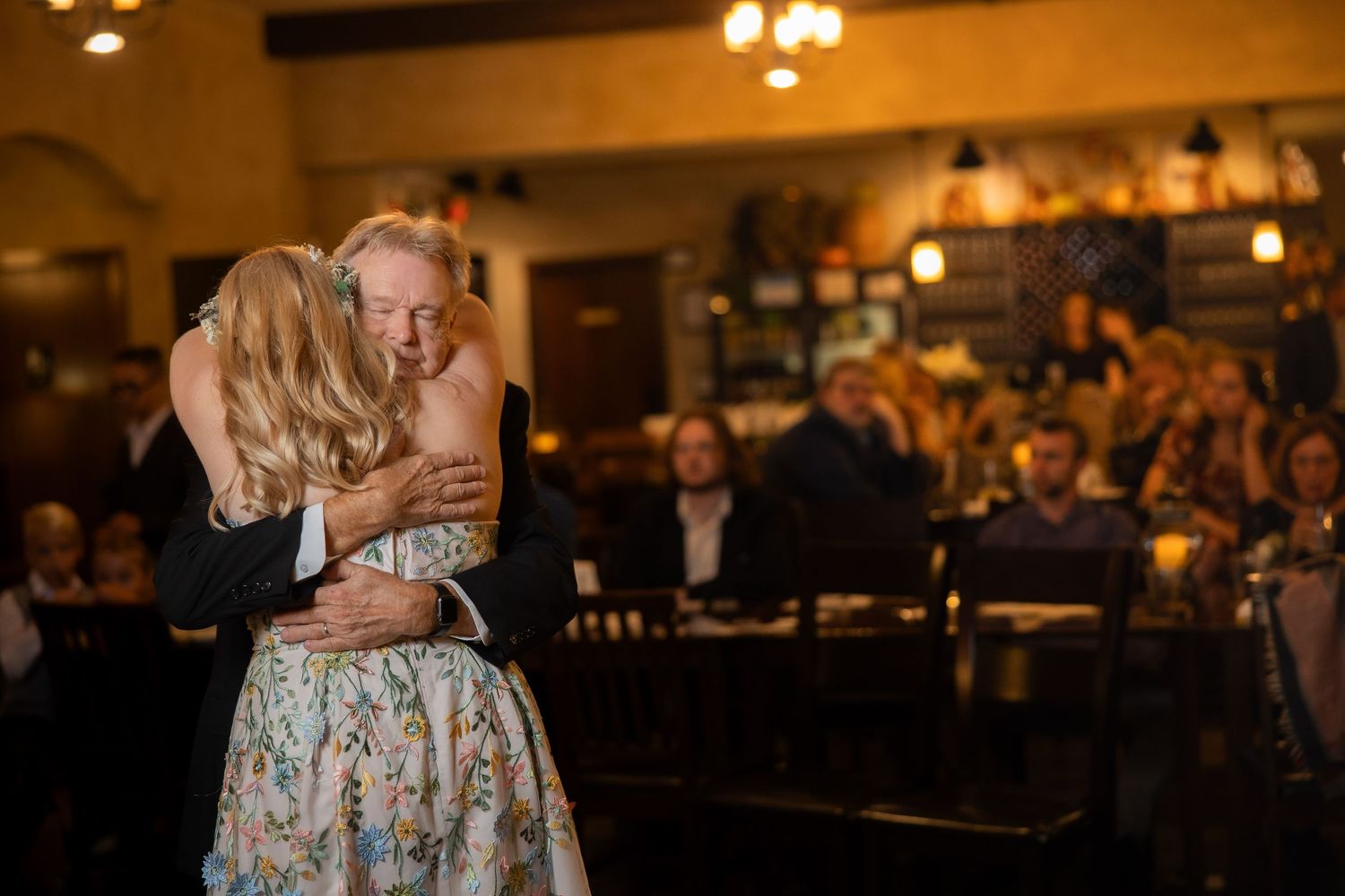 Couple dances together in an elegantly lit reception hall with wooden beams.