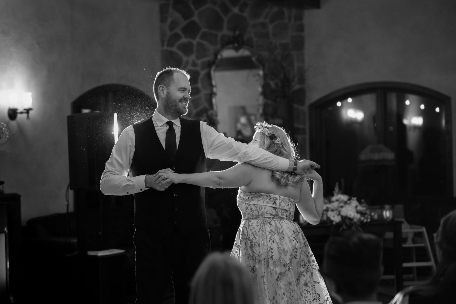 A couple shares an intimate dance together in black and white at an elegant venue with arched doorways and mood lighting.