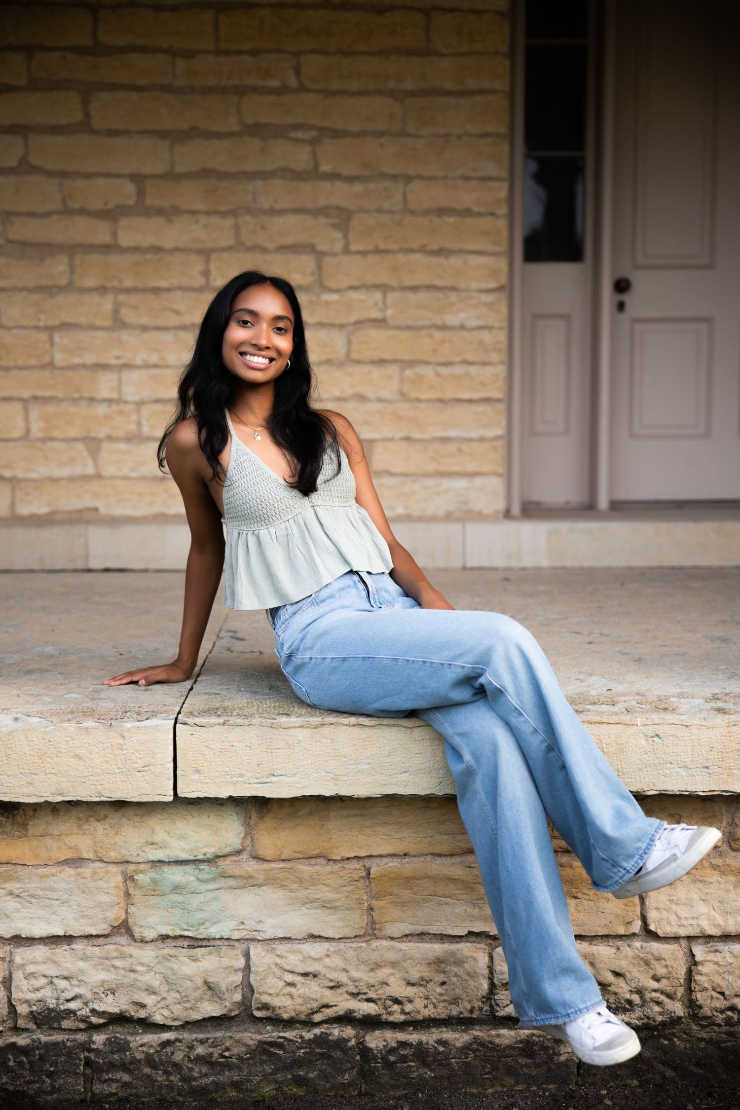 Person in light top and jeans lounging on stone steps against beige brick wall.