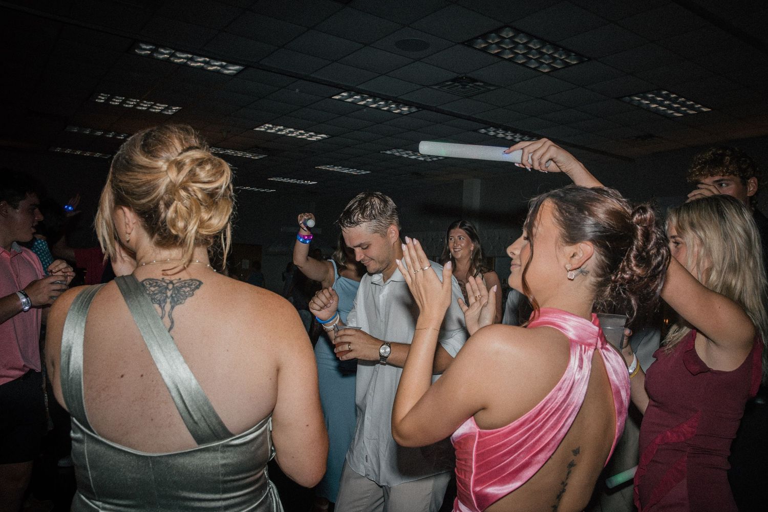 Wedding reception dance floor with guests dancing, including bride in white gown and woman in pink dress.