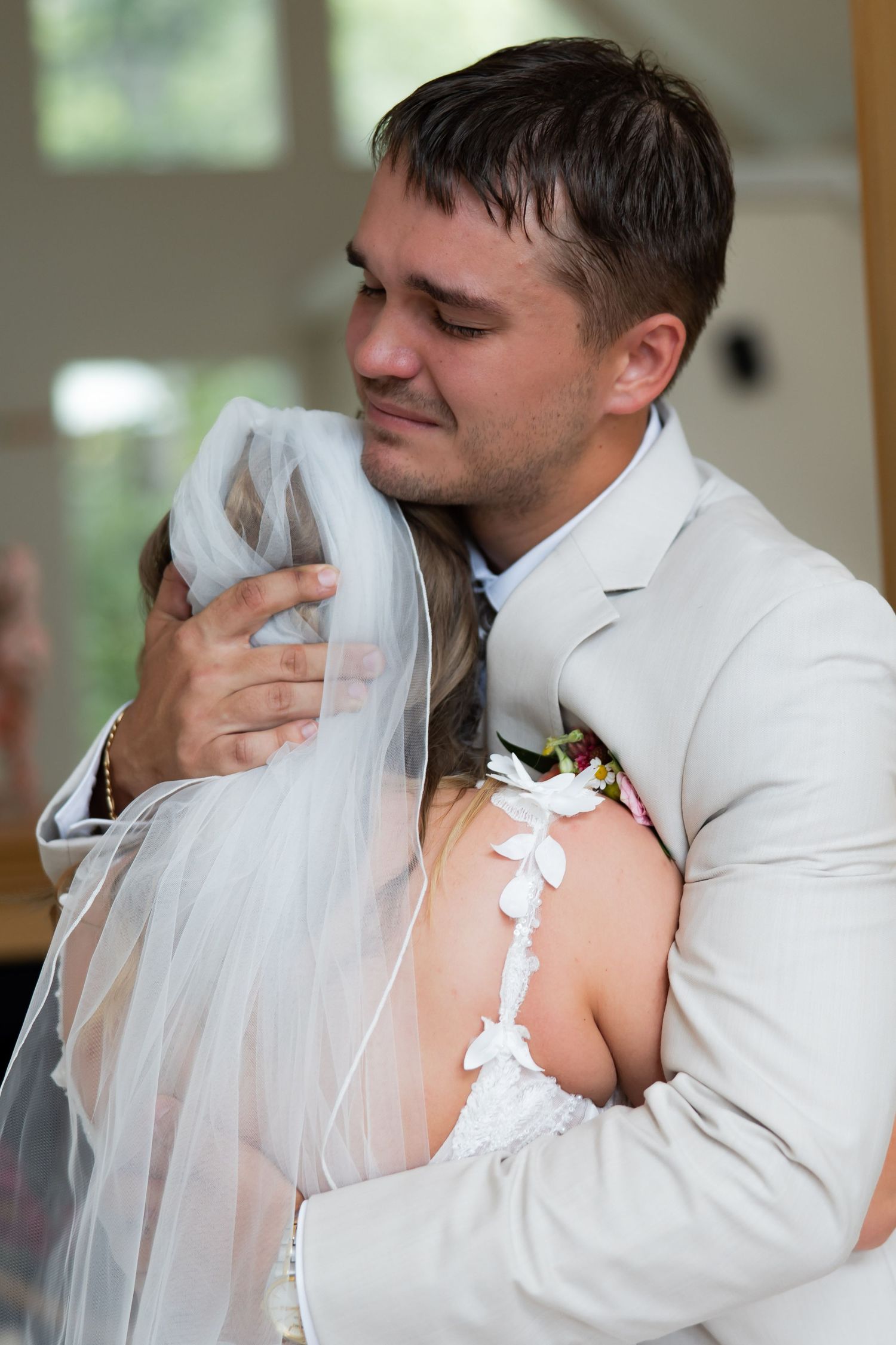 Emotional groom embracing bride in wedding dress and veil during first look.