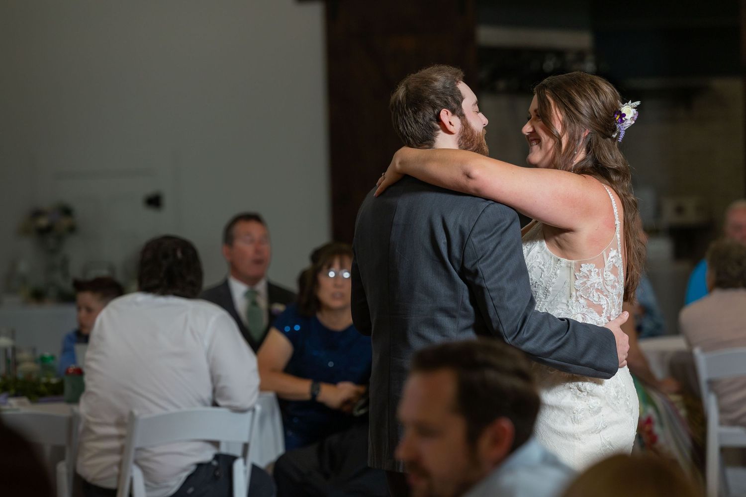 Bride and groom share their first dance at wedding reception while guests watch in background.