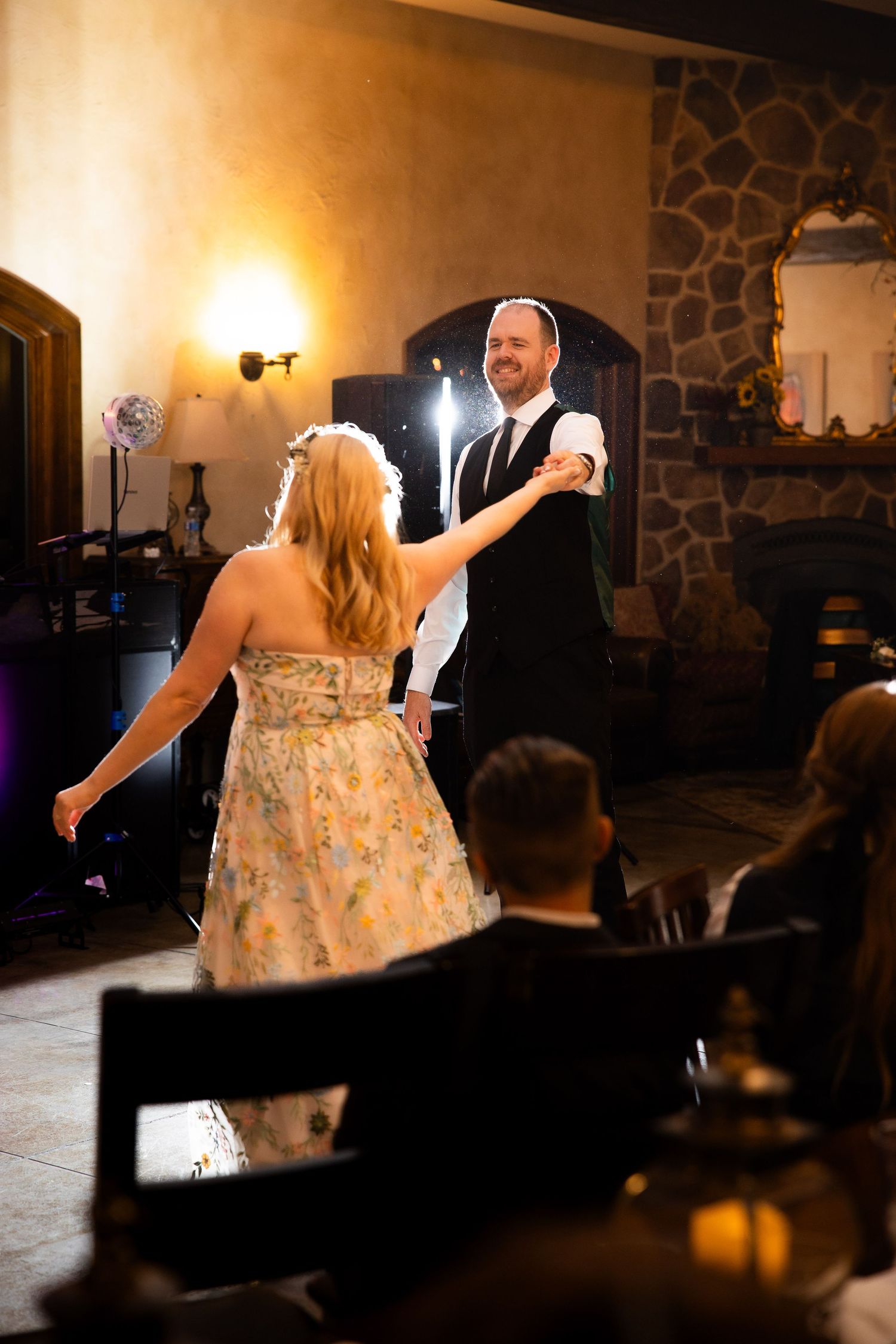 A couple shares a romantic dance in a rustic stone-walled venue with warm lighting.