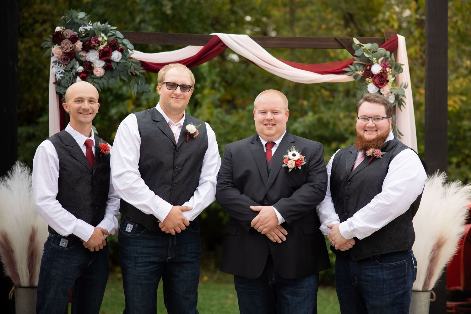 A wedding party in formal attire poses together outdoors wearing navy vests and white shirts.