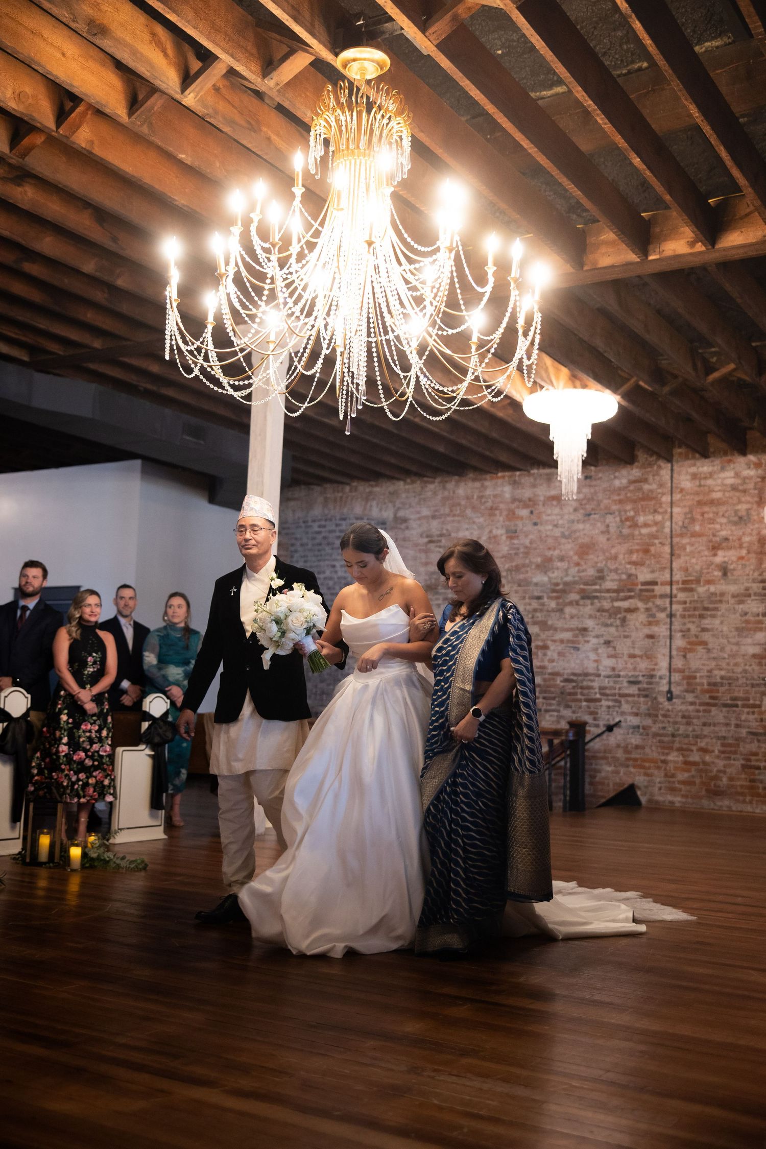 Wedding party dancing in a rustic brick venue with elegant chandeliers overhead.