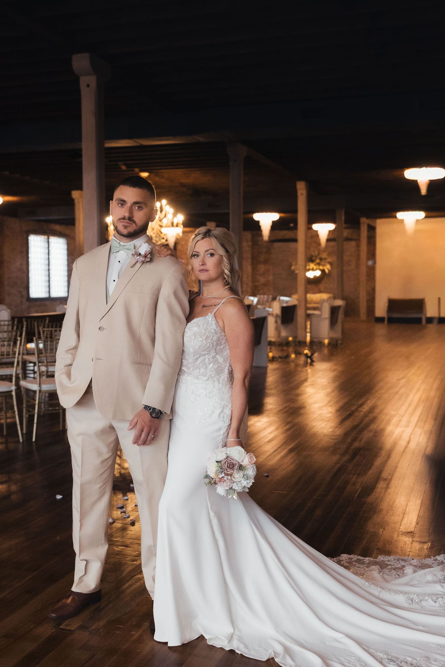 A couple poses in an elegant wedding venue with exposed brick walls and hardwood floors.