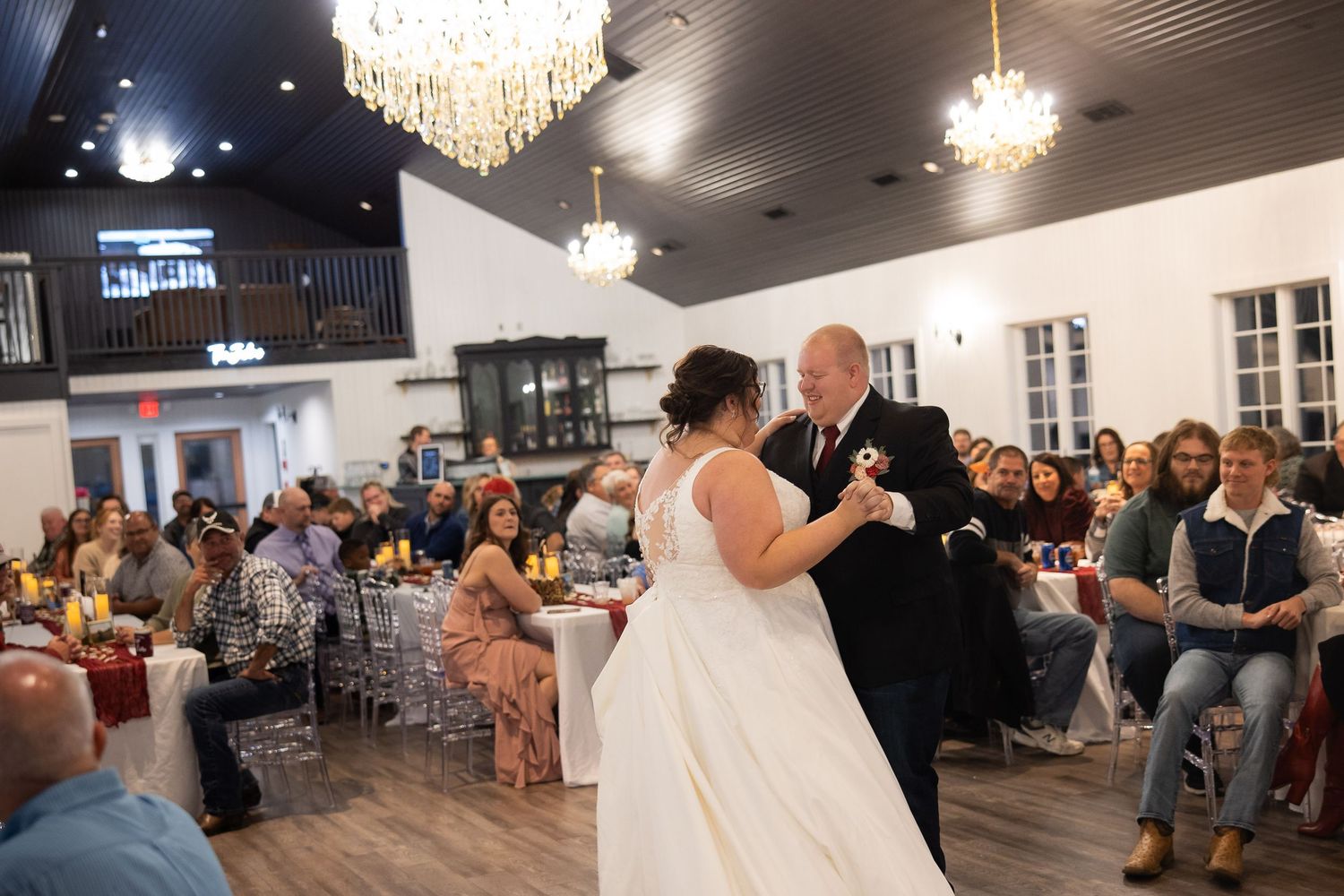 Wedding reception guests dance under elegant crystal chandeliers in a spacious ballroom.