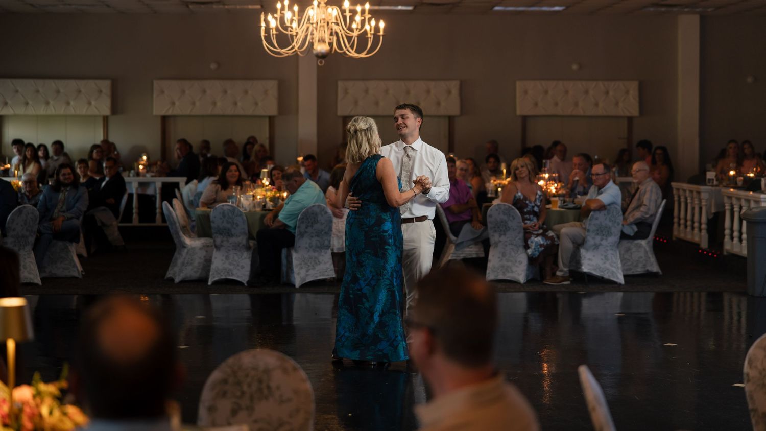 Couple shares special dance moment in candlelit wedding reception ballroom with seated guests.