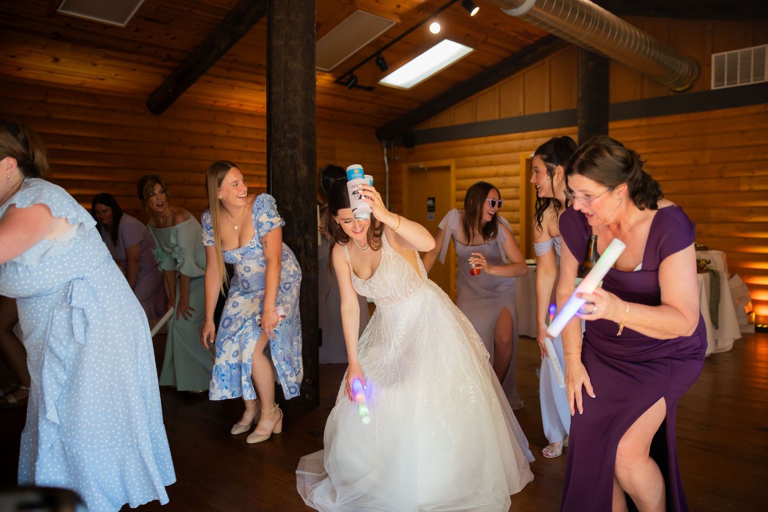 Bride dances joyfully with bridesmaids holding glow sticks on the dance floor at a rustic barn wedding.