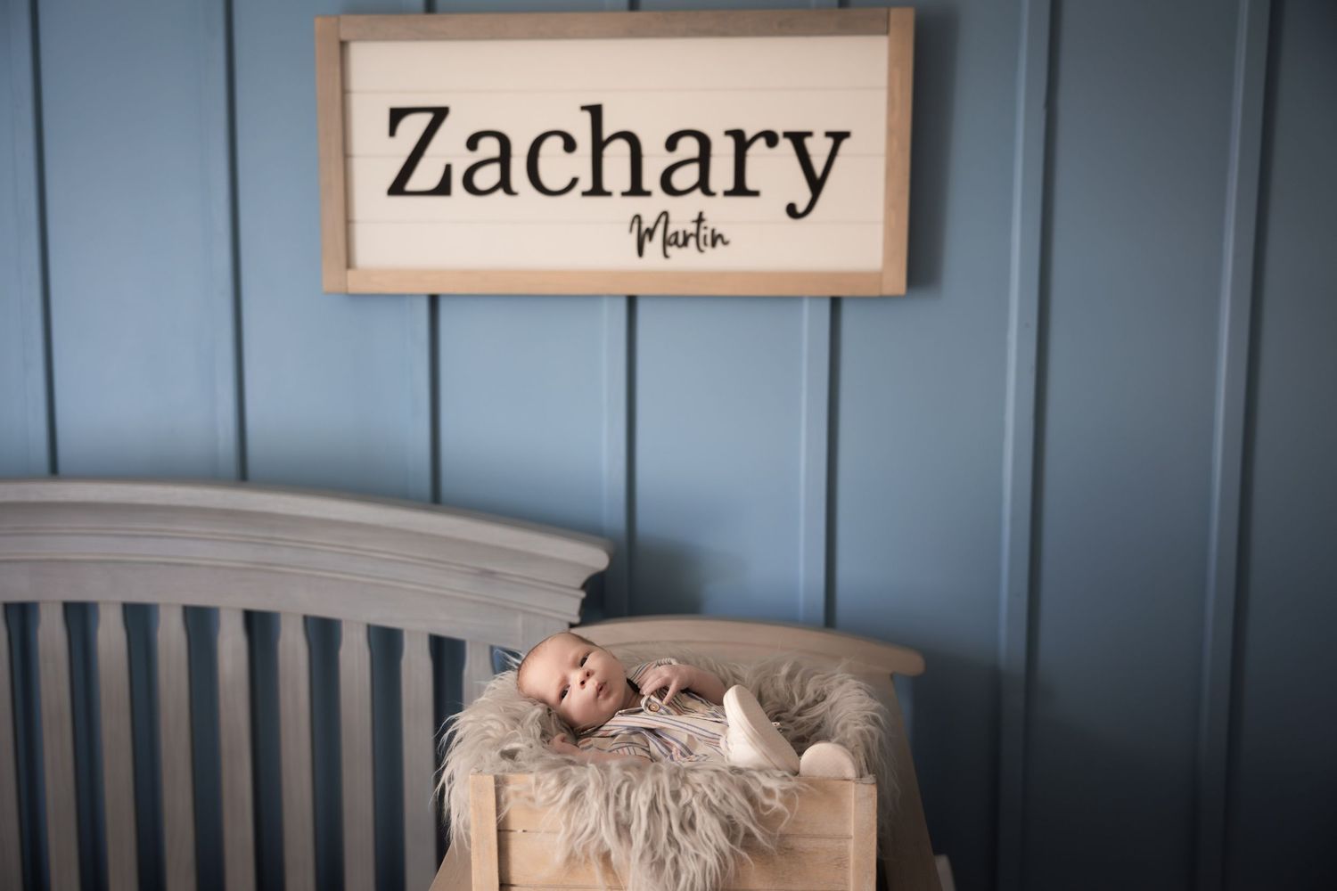 Blue nursery wall with wooden name sign and decorative elements.