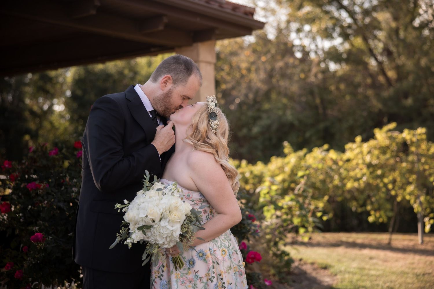 A romantic outdoor wedding dance captured at sunset under a covered patio with blooming flowers.