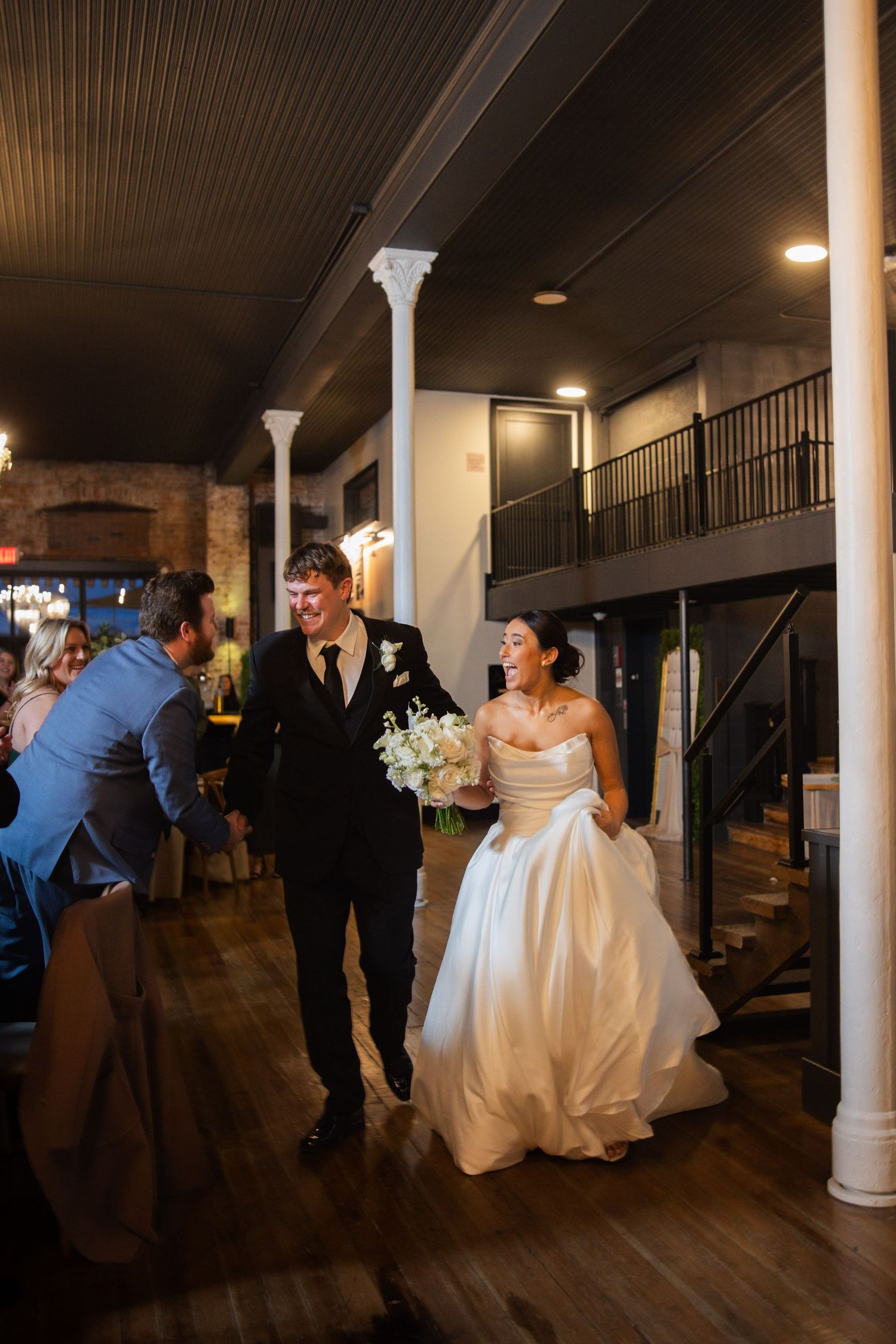 Wedding party moving through dimly lit venue with white columns and hardwood floors.