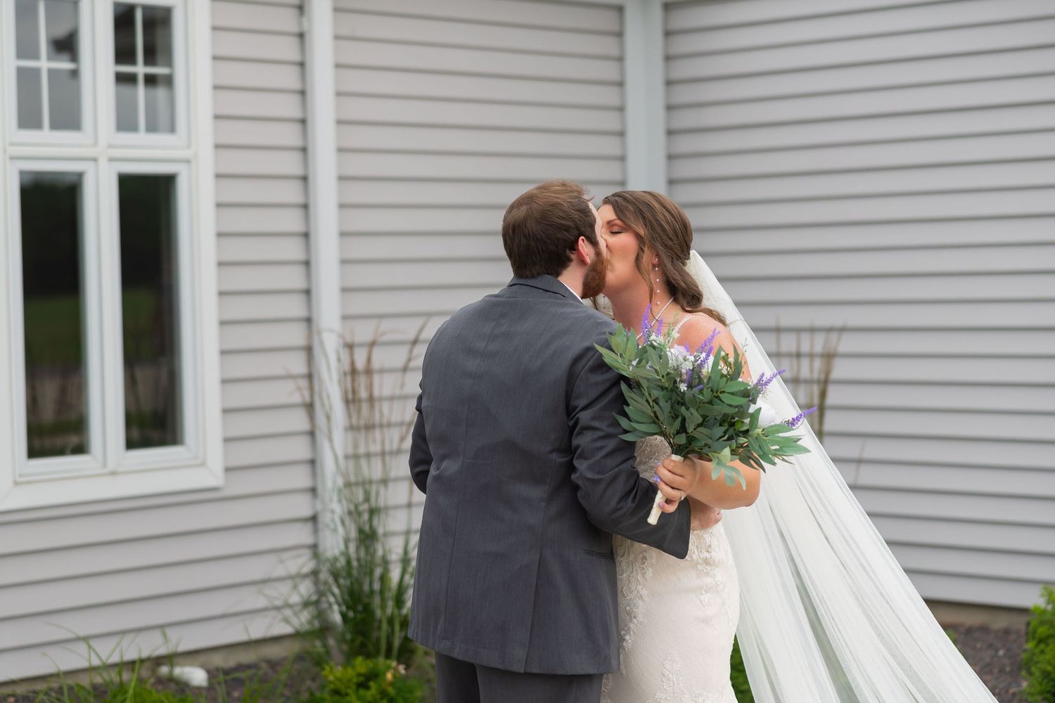 Bride and groom sharing a kiss outdoors, bride holding a lush green and pink bouquet.