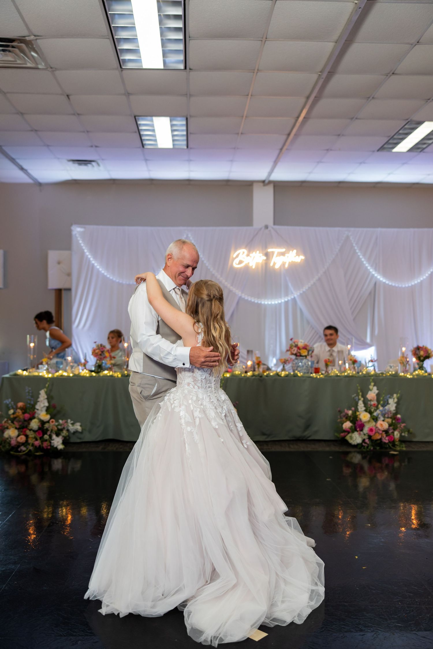 Bride in white lace gown shares father-daughter dance at elegant wedding reception.