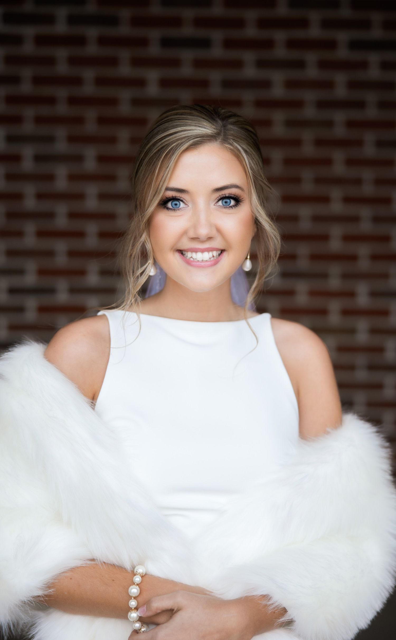 Bridal portrait with white fur wrap against brick wall background.