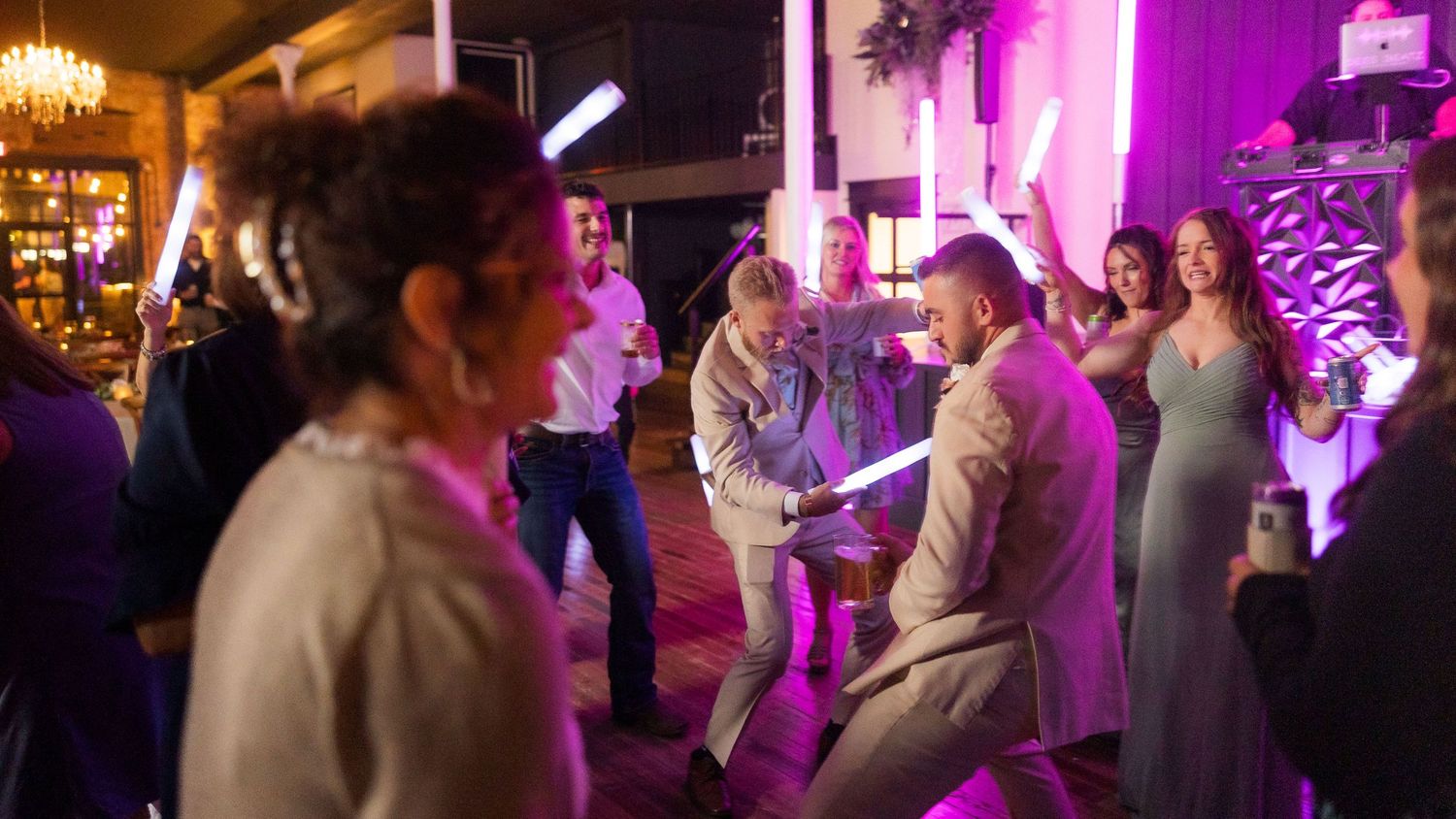 Wedding reception dance party with purple uplighting and chandeliers creating a festive atmosphere.