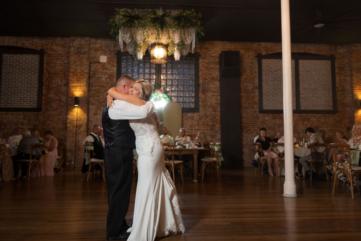 A couple shares their first dance in an elegant reception venue with exposed brick walls and warm lighting.