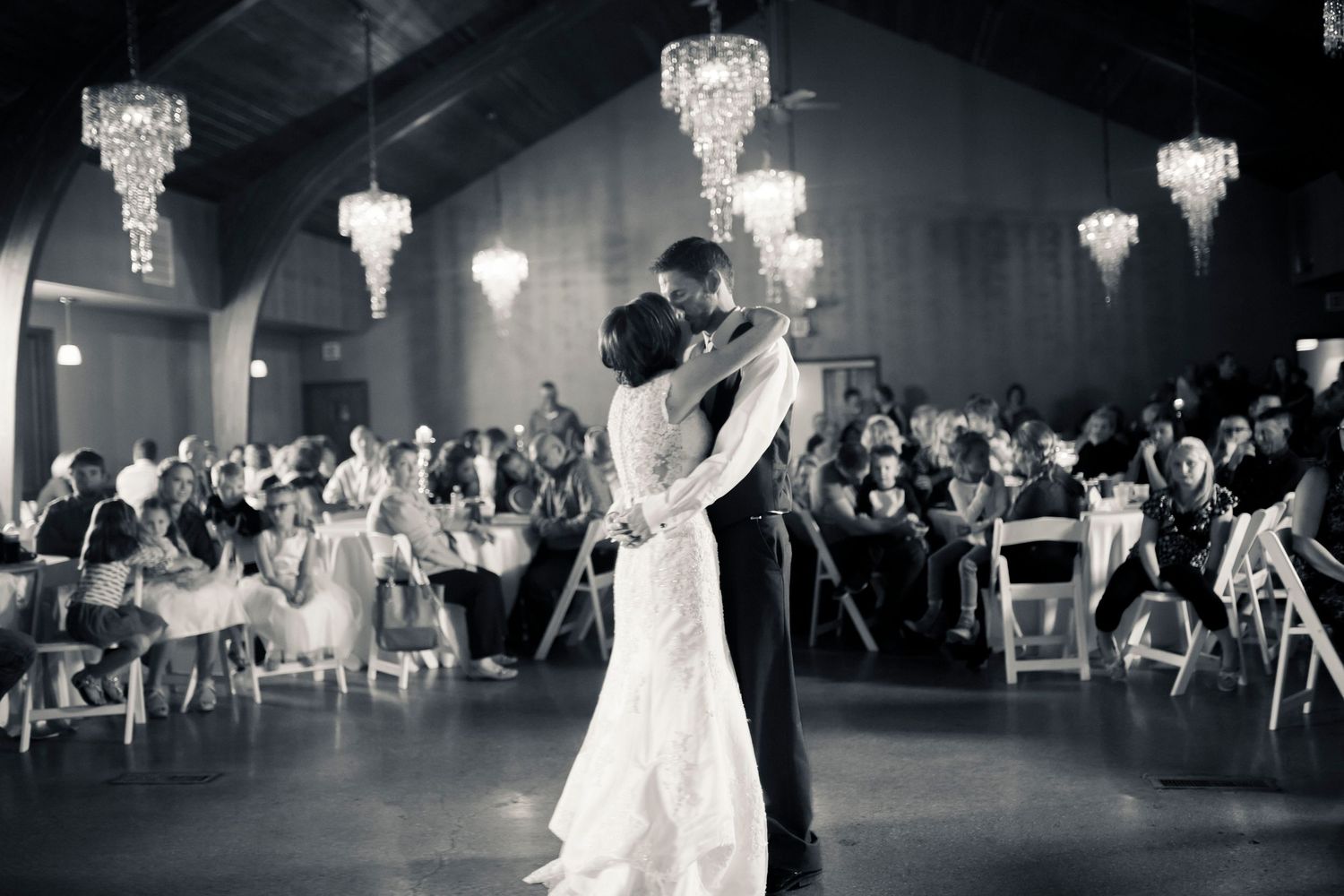 Black and white reception hall scene with crystal chandeliers and dancing guests.