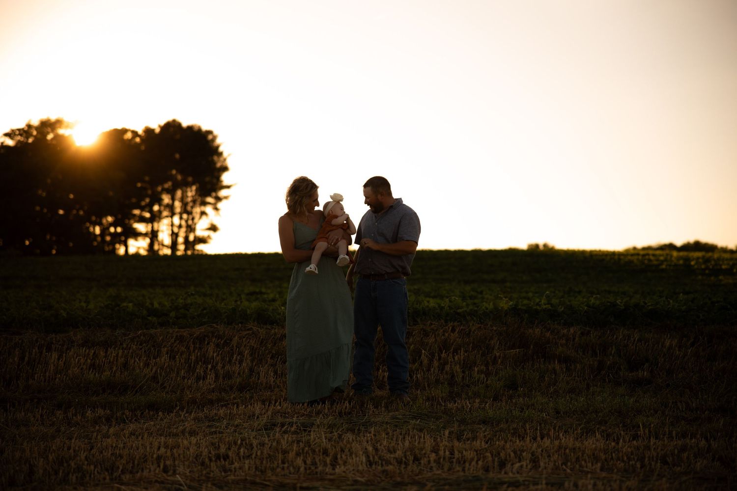 Silhouettes of people standing against golden sunset sky in field.