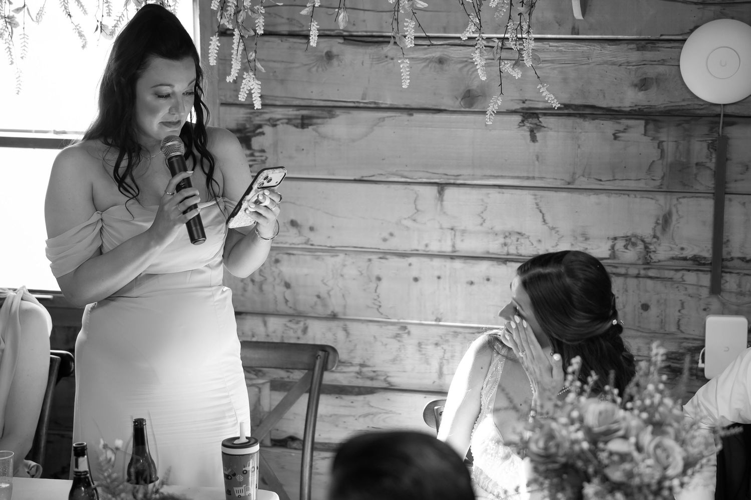 Black and white photo of a woman giving a heartfelt wedding speech at a rustic barn reception.