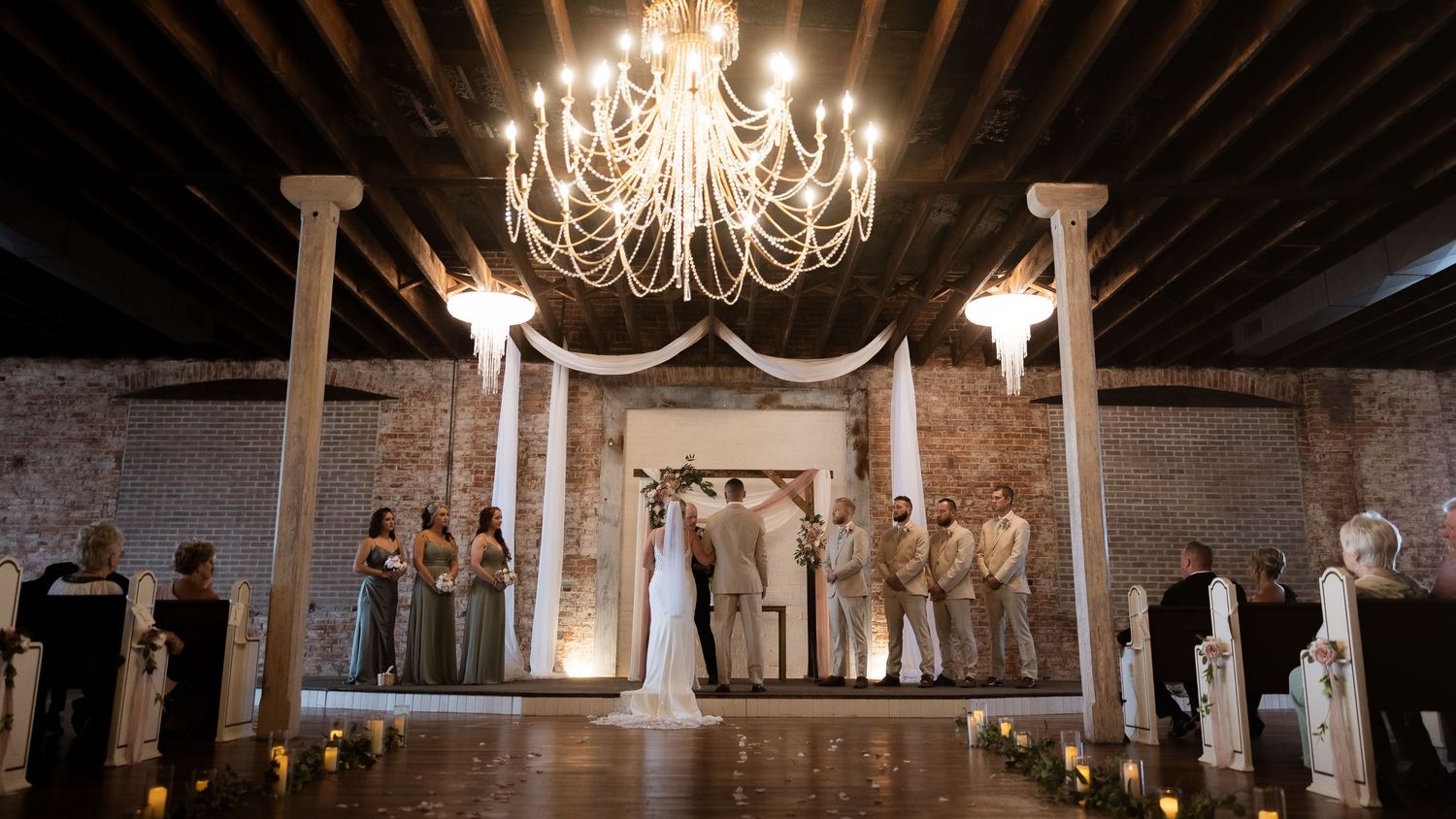 A panoramic view of an elegant wedding venue with chandeliers and exposed brick walls.