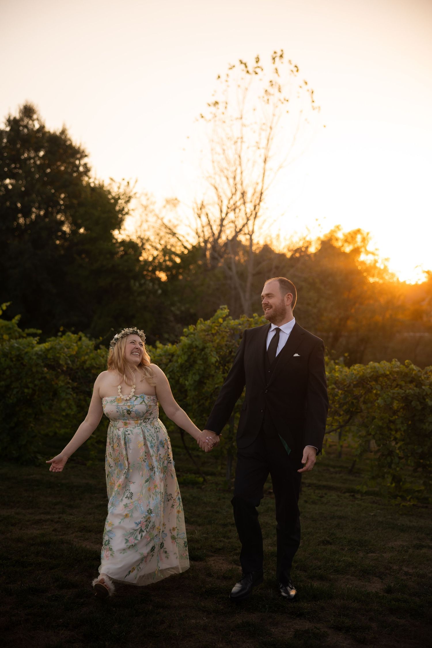 Couple walks hand in hand through vineyard at golden hour.
