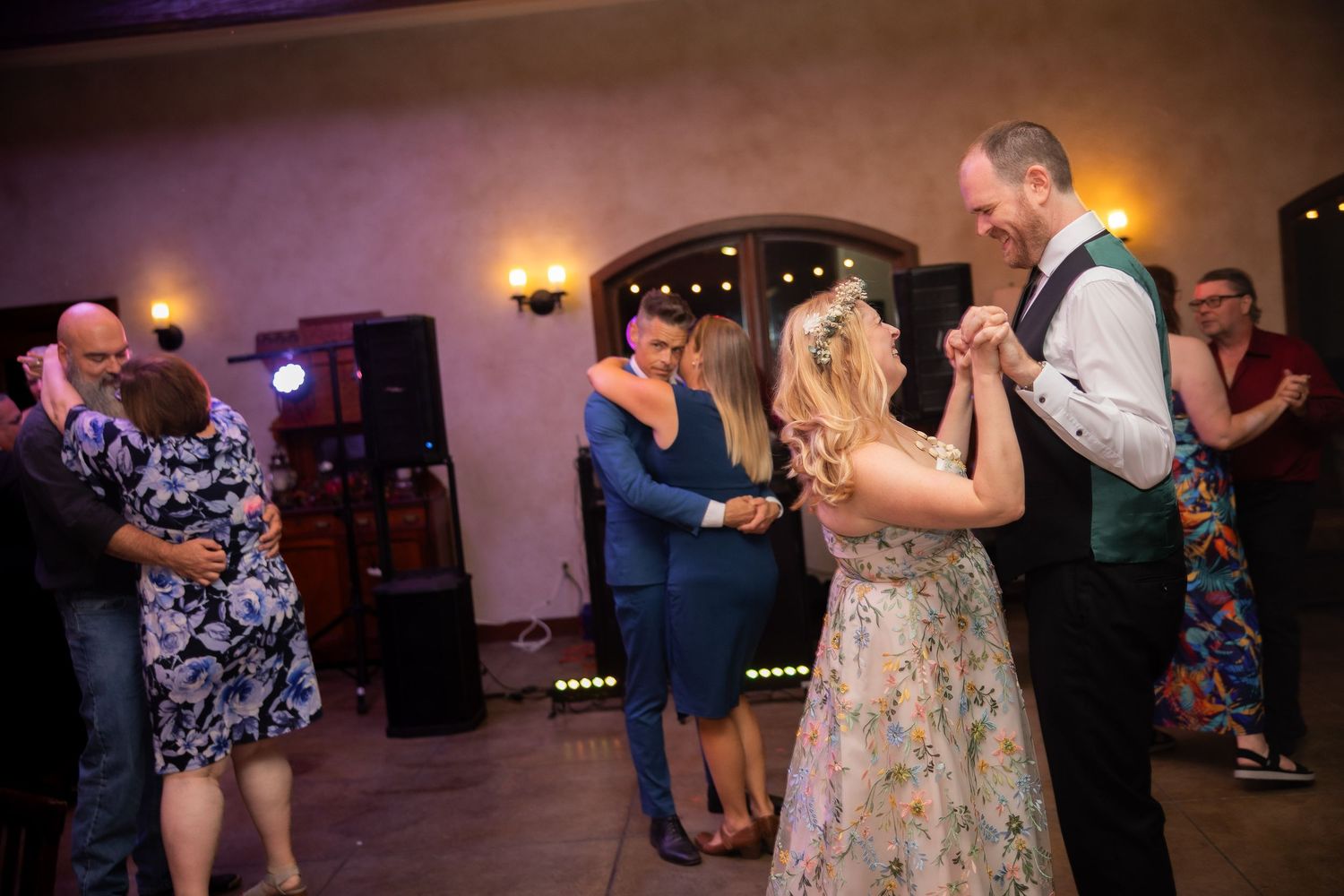 Couples dancing together at a wedding reception in a warmly lit ballroom venue.