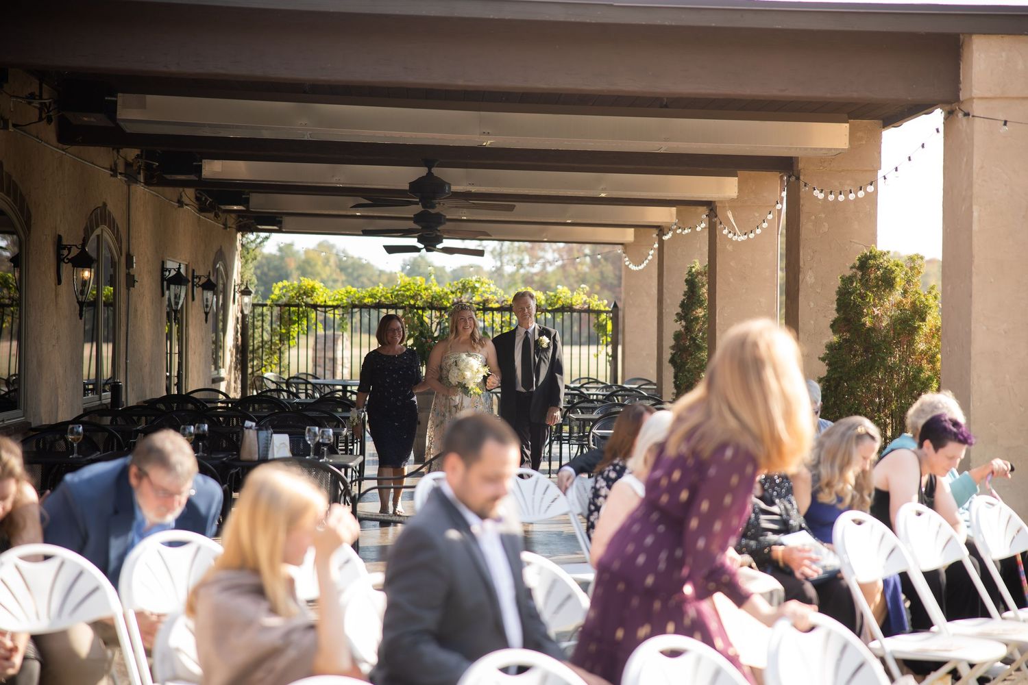 Wedding guests gather under a covered outdoor patio area decorated with pink flowers.