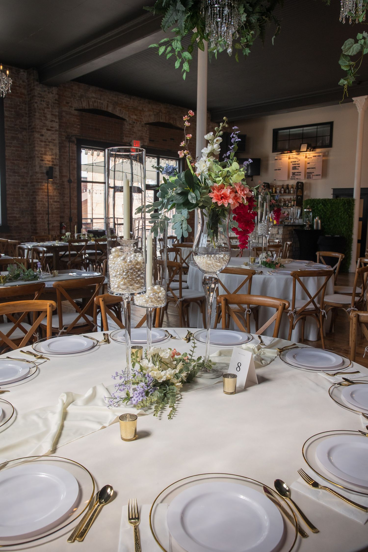 Elegant wedding reception table settings with white linens and floral centerpieces in an industrial venue.