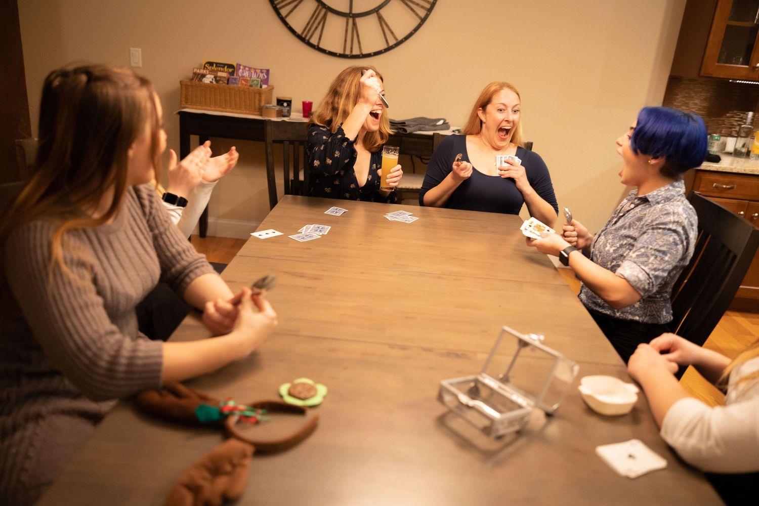 Group gathered around wooden table playing cards in warm indoor lighting.