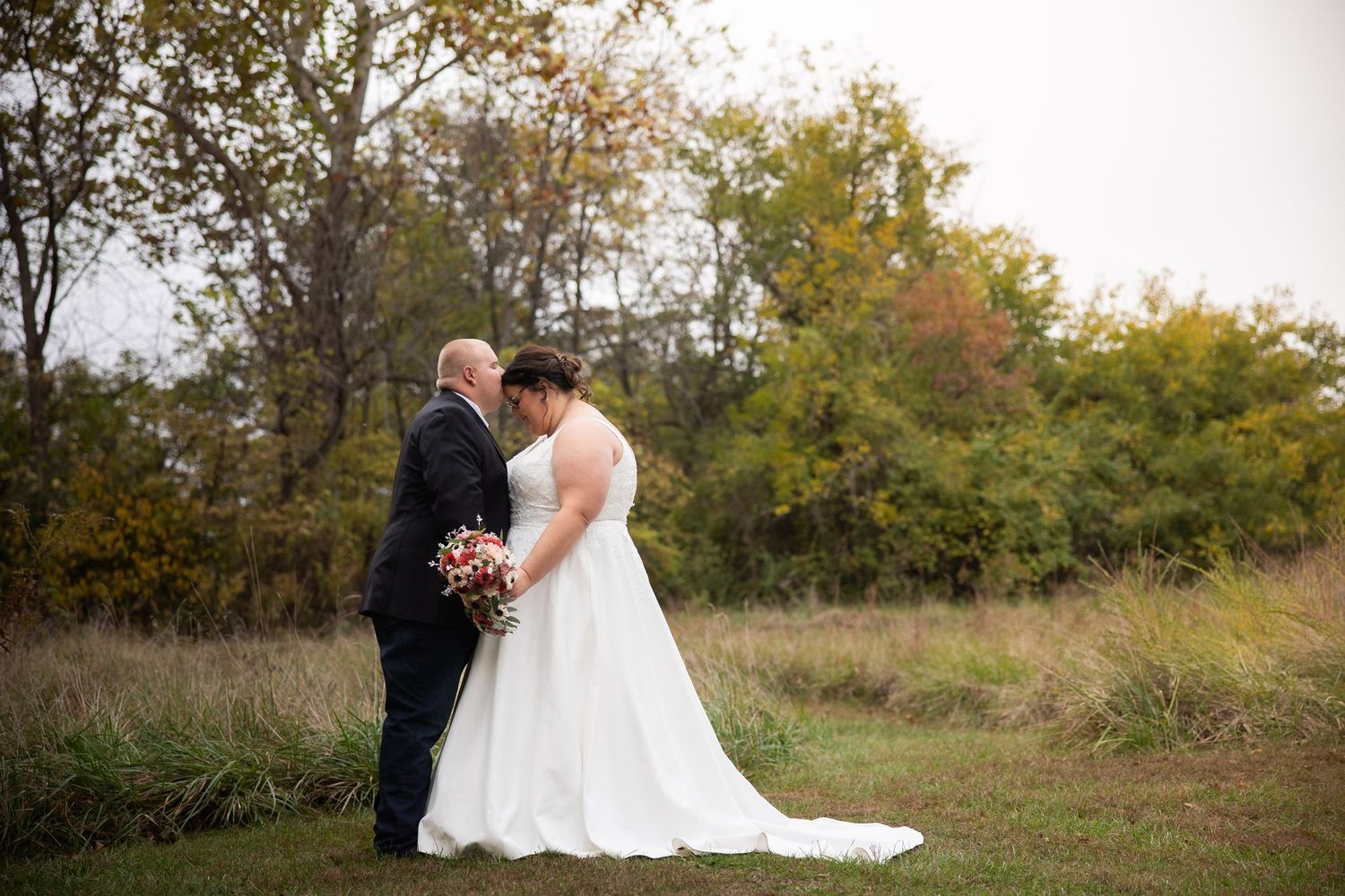 Romantic silhouette of newlyweds against autumn foliage in outdoor wedding setting.