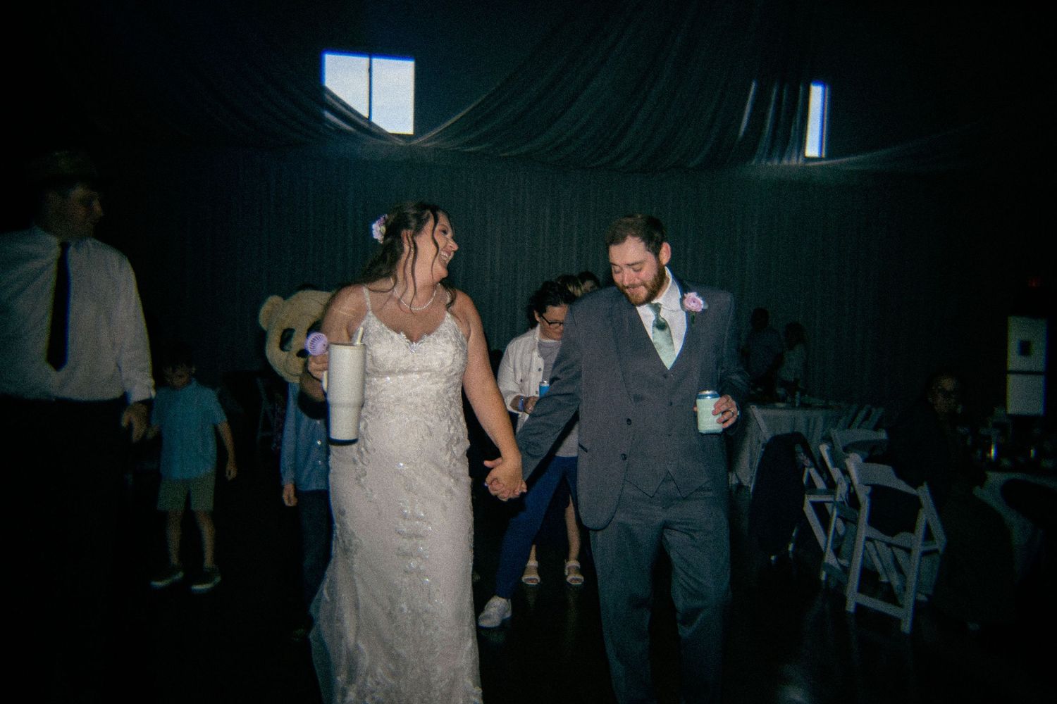Bride and groom hold hands dancing at their wedding reception in a dimly lit venue.
