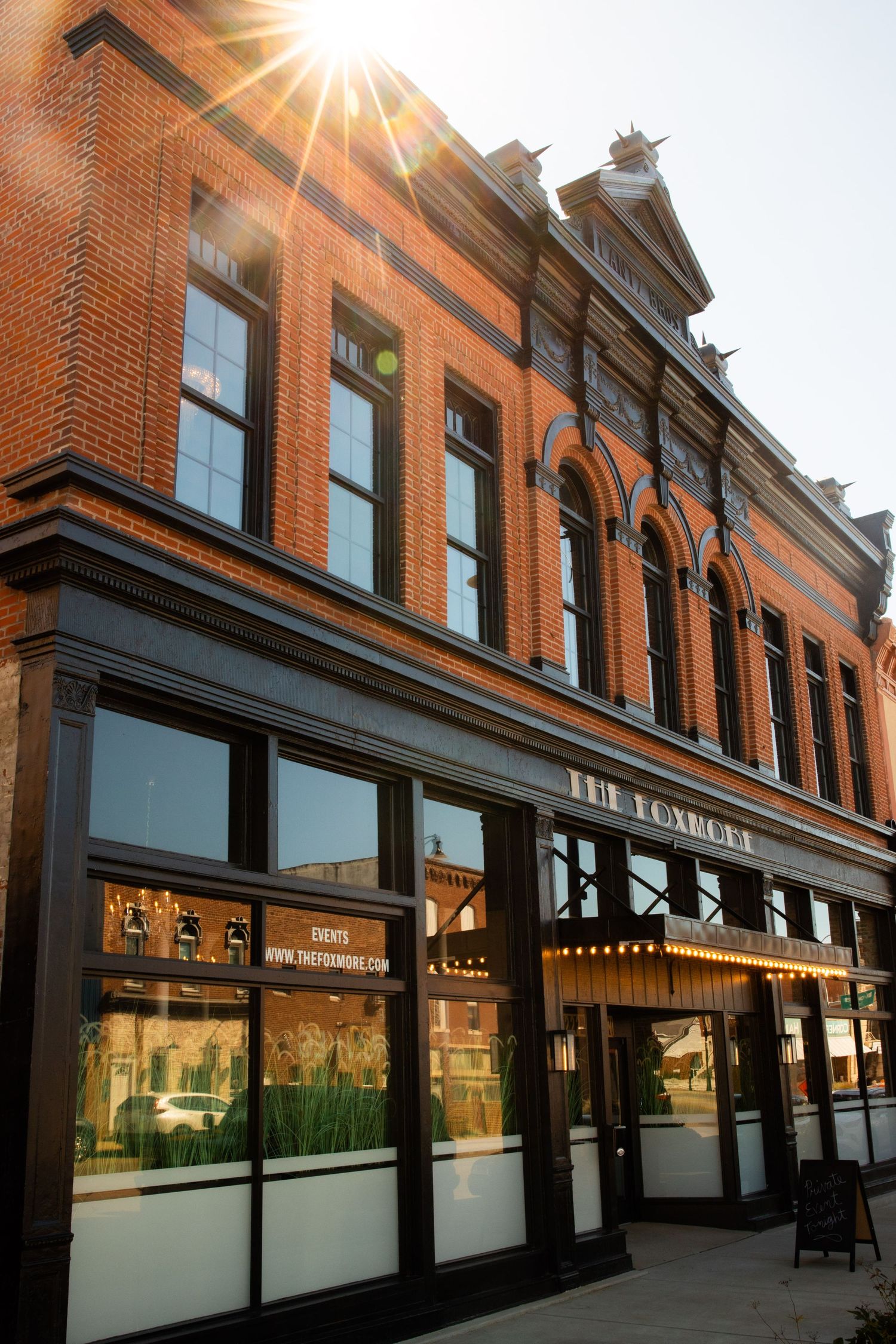 Exterior of The Foxhole brick building with arched windows, ornate facade, and warm sunburst light on a city street.