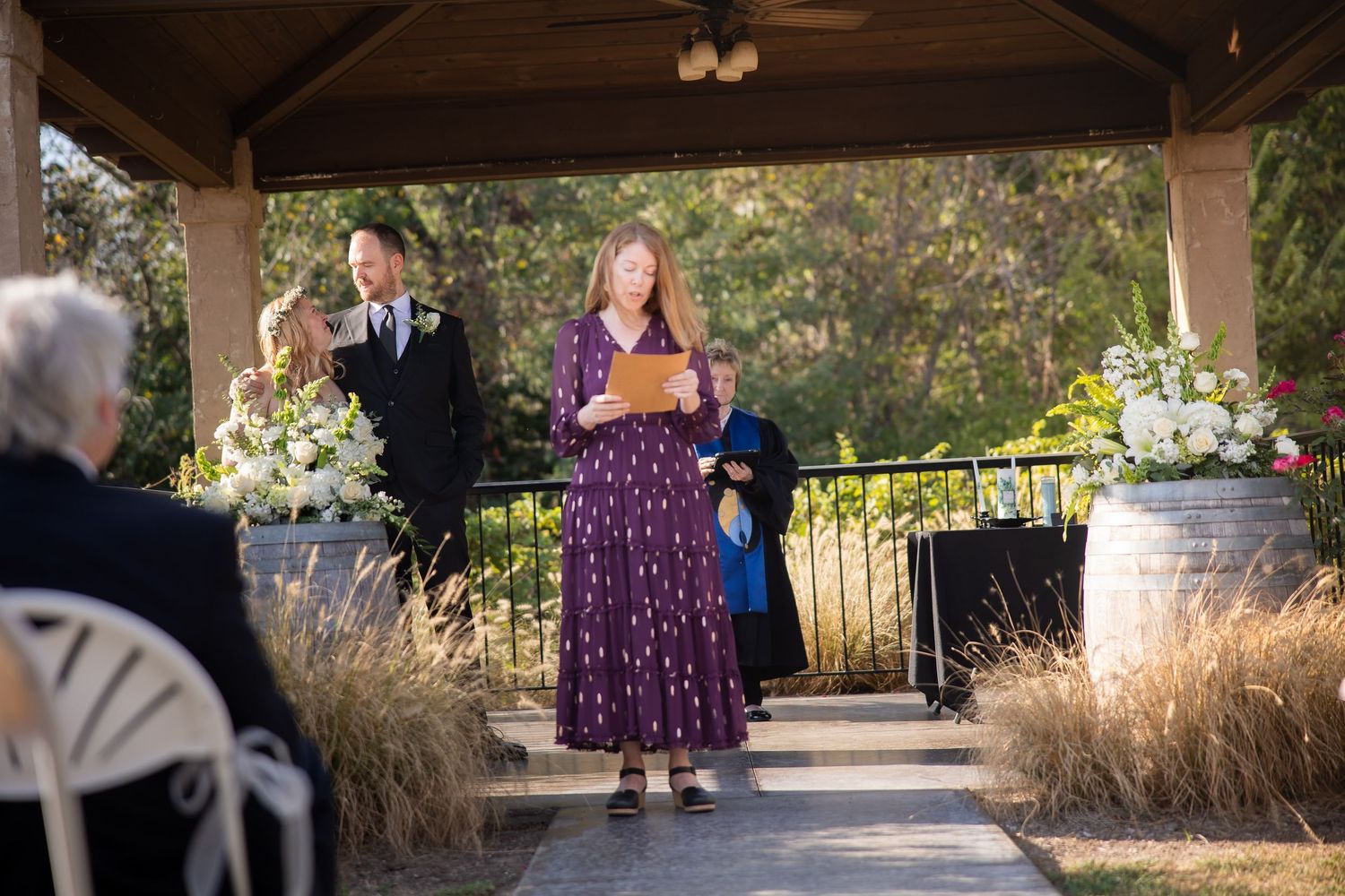 A couple poses together under a covered outdoor area with stone columns during a wedding ceremony.