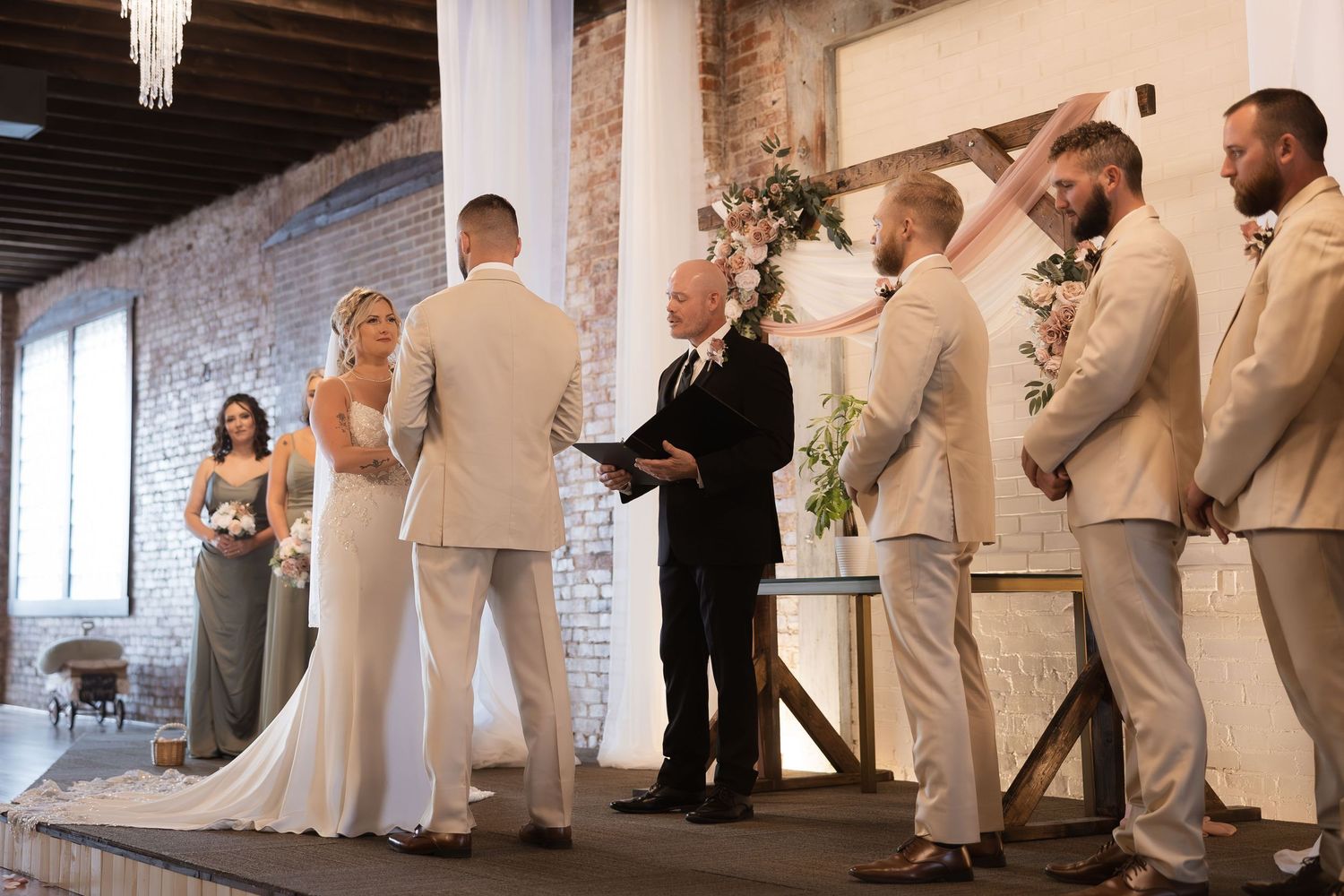 Wedding ceremony in progress at industrial venue with exposed brick walls and elegant white decor.