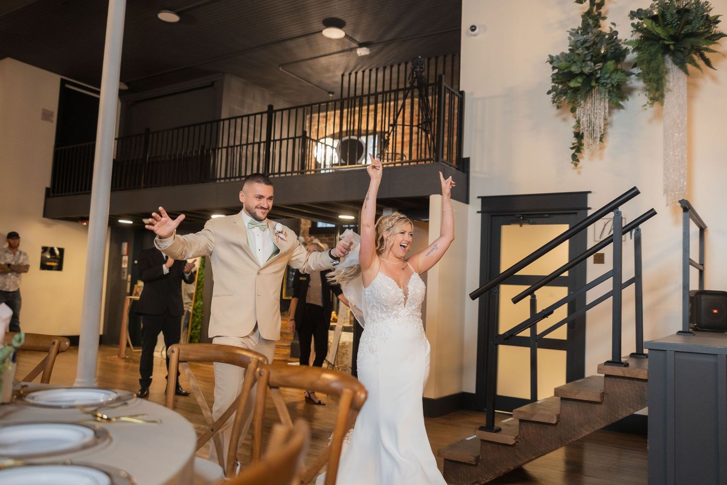 A couple celebrates with raised arms during their wedding reception in an industrial-style venue.
