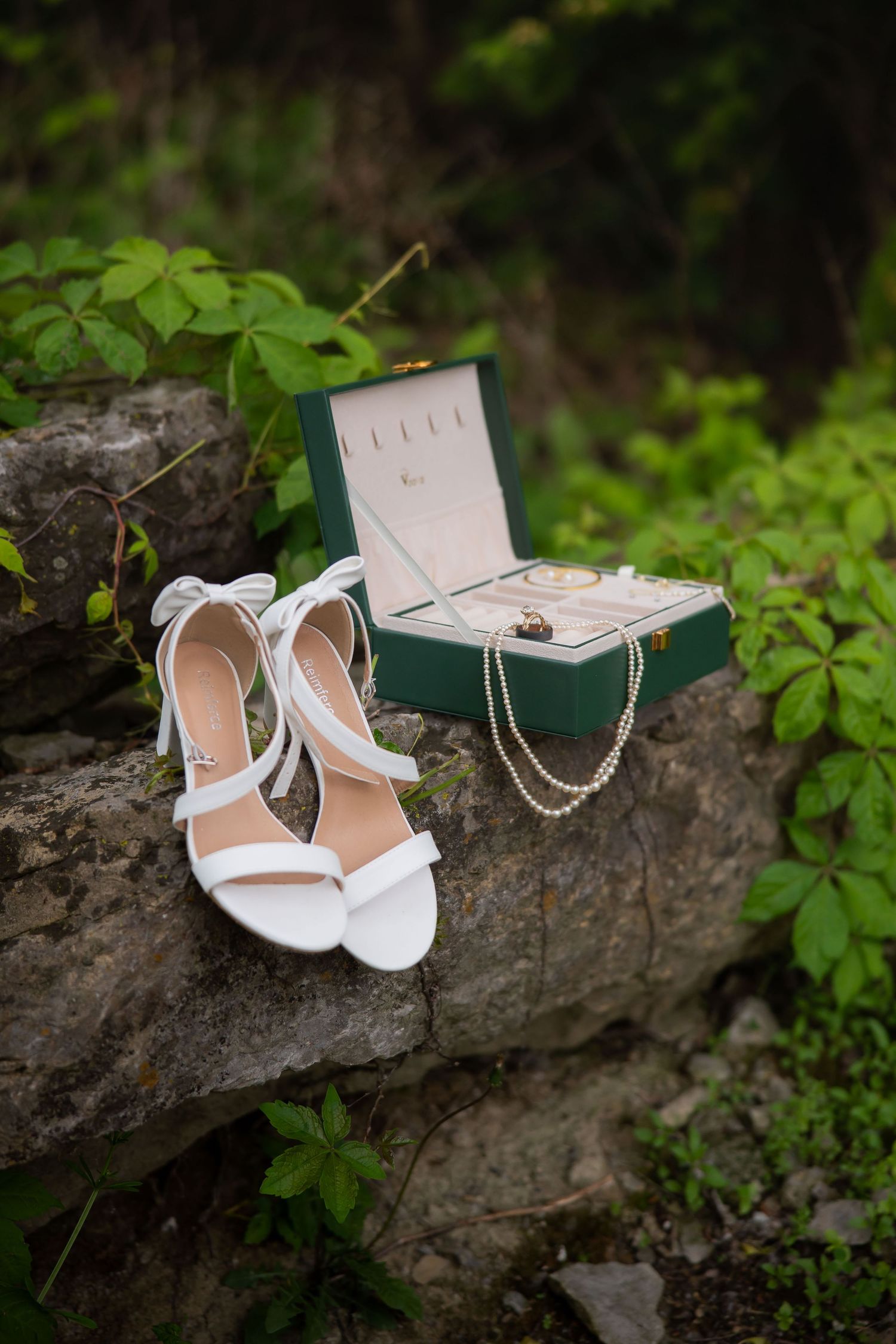 White bridal heels and green jewelry box with pearl necklace and ring displayed on rustic stone steps.