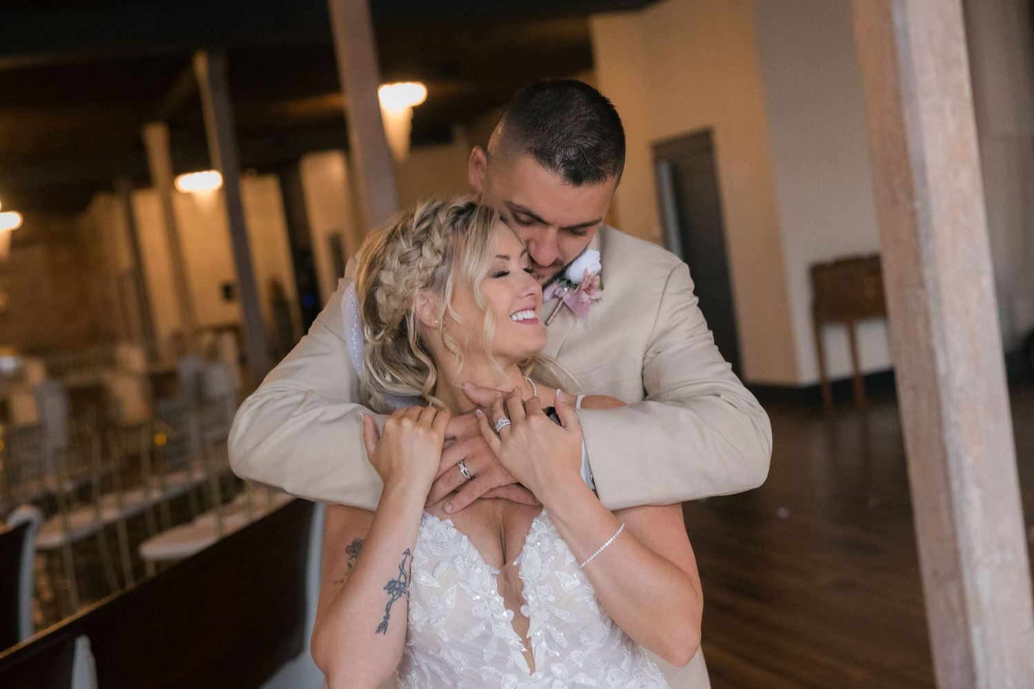 Couple shares intimate moments during wedding photoshoot in rustic indoor venue with warm lighting.
