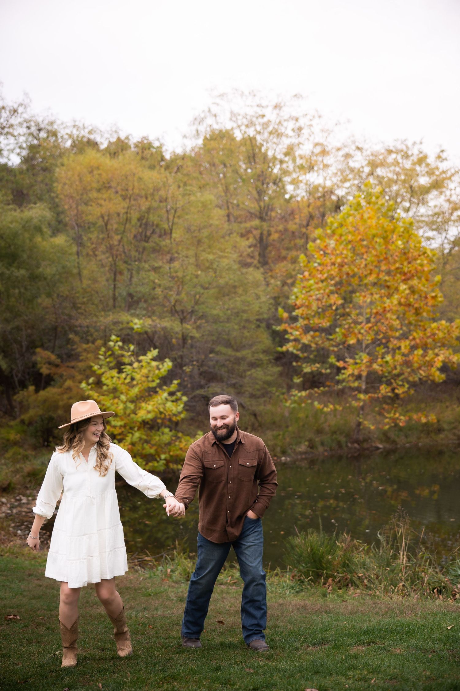 Two people share a playful moment in a field surrounded by autumn trees with golden foliage.