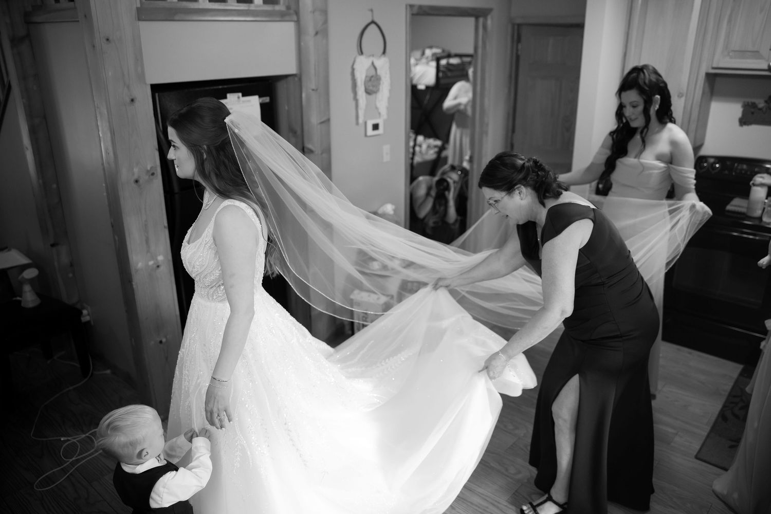 Bridesmaids helping bride with long veil and wedding dress in black and white photo.