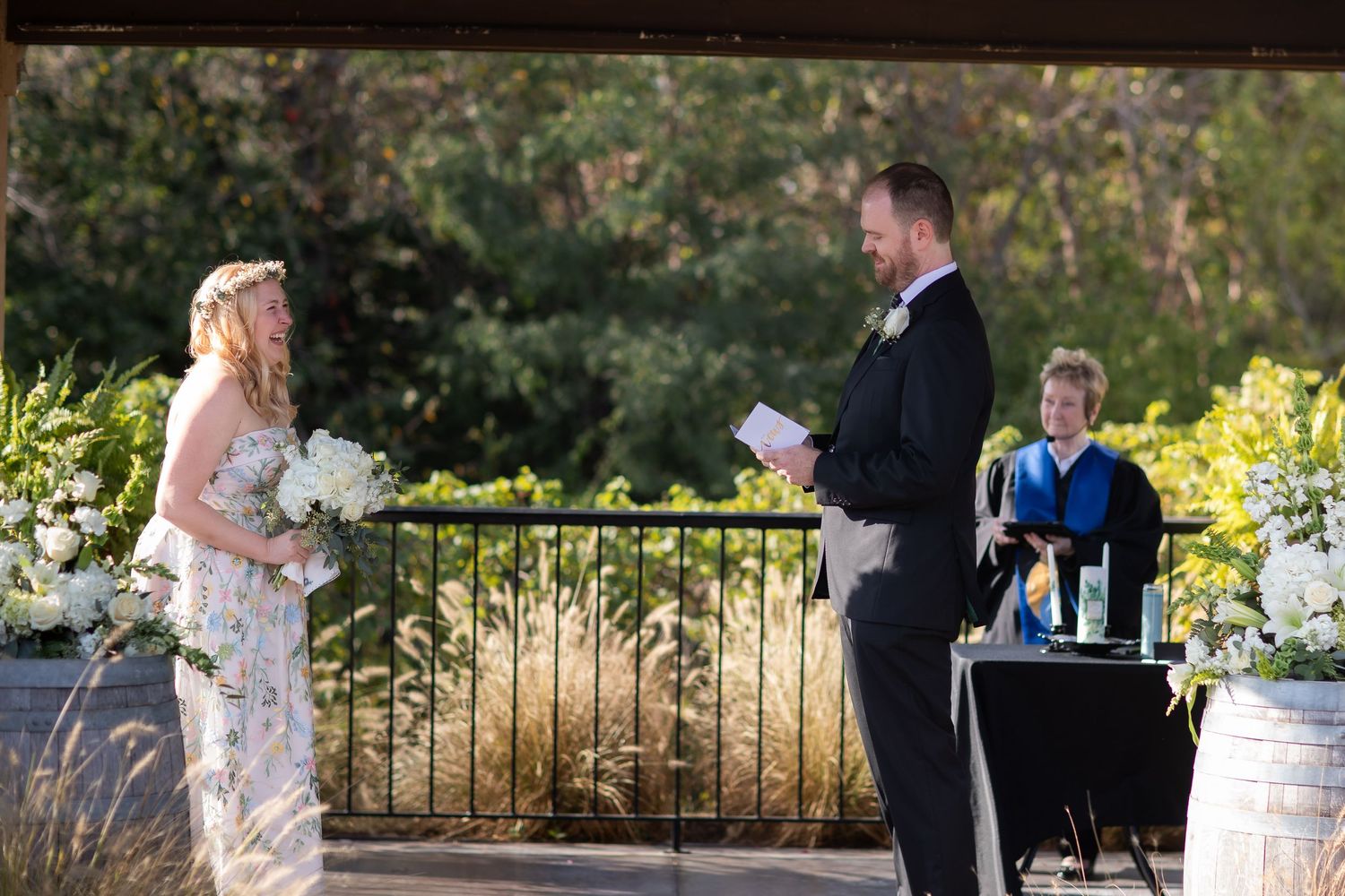 A wedding couple stands together on a stone patio surrounded by autumn foliage and flowers.
