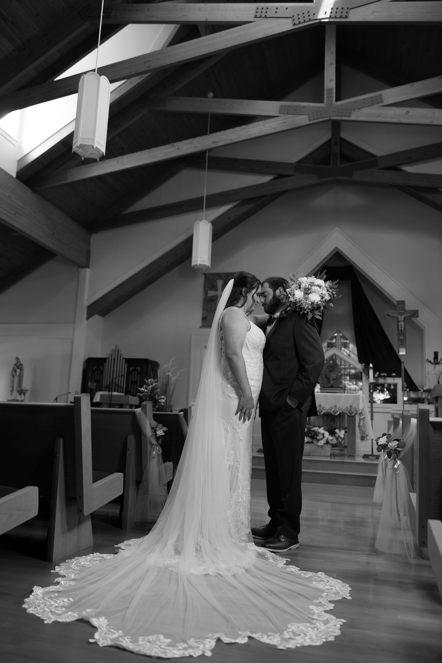 Black and white photo of a bride and groom sharing their first kiss at the altar inside a wooden church.