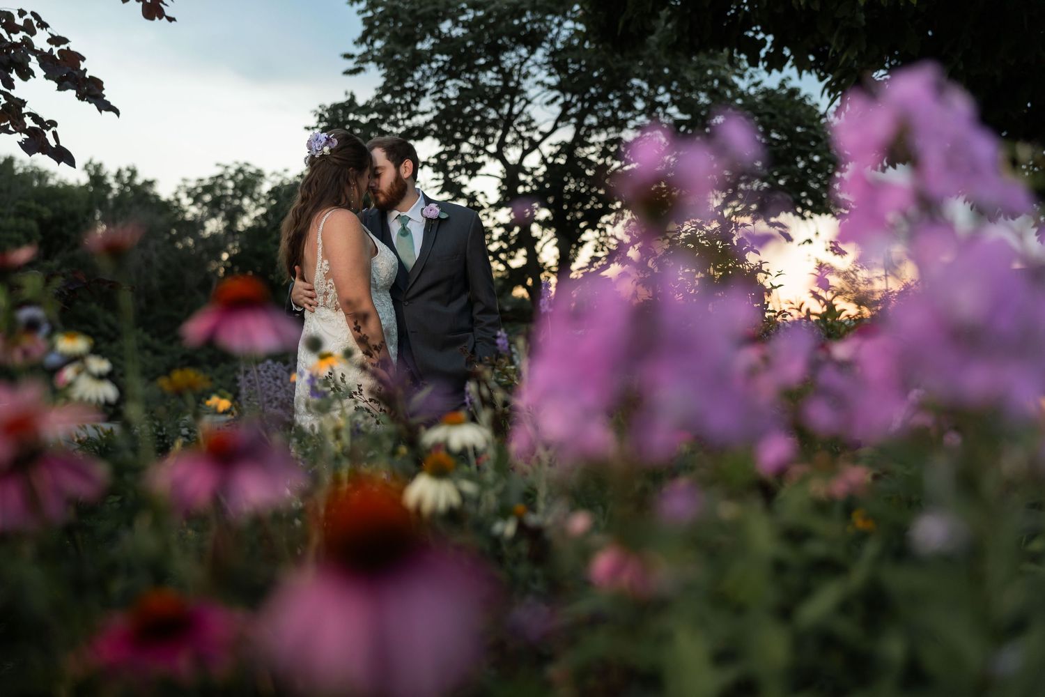 Couple sharing a romantic moment at sunset surrounded by colorful wildflowers in a lush garden setting.
