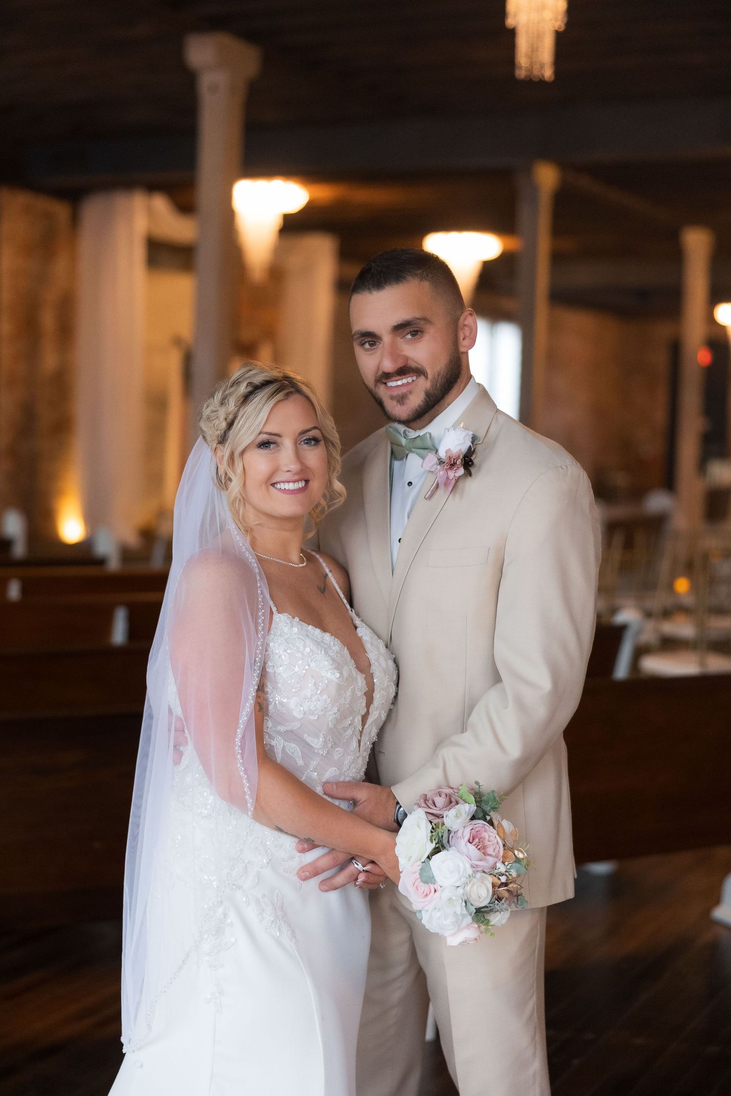 A romantic wedding couple shares a tender moment in a rustic indoor venue with exposed brick walls and warm lighting.