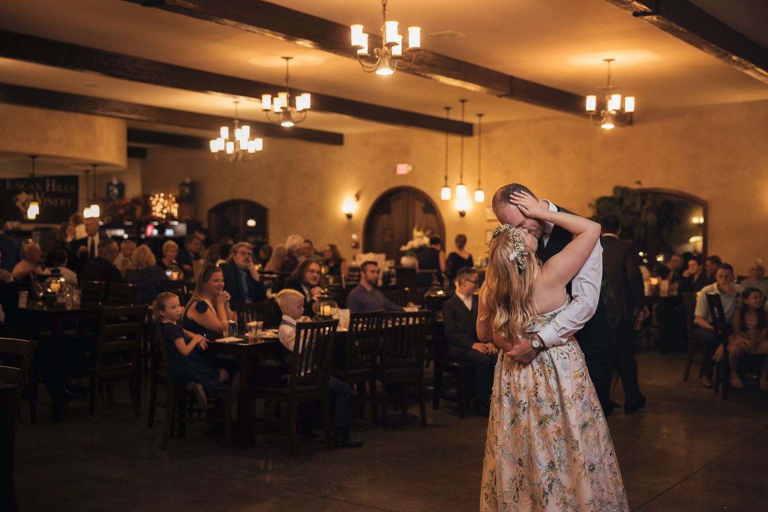 Couples slow dancing in an elegant ballroom with chandeliers overhead.