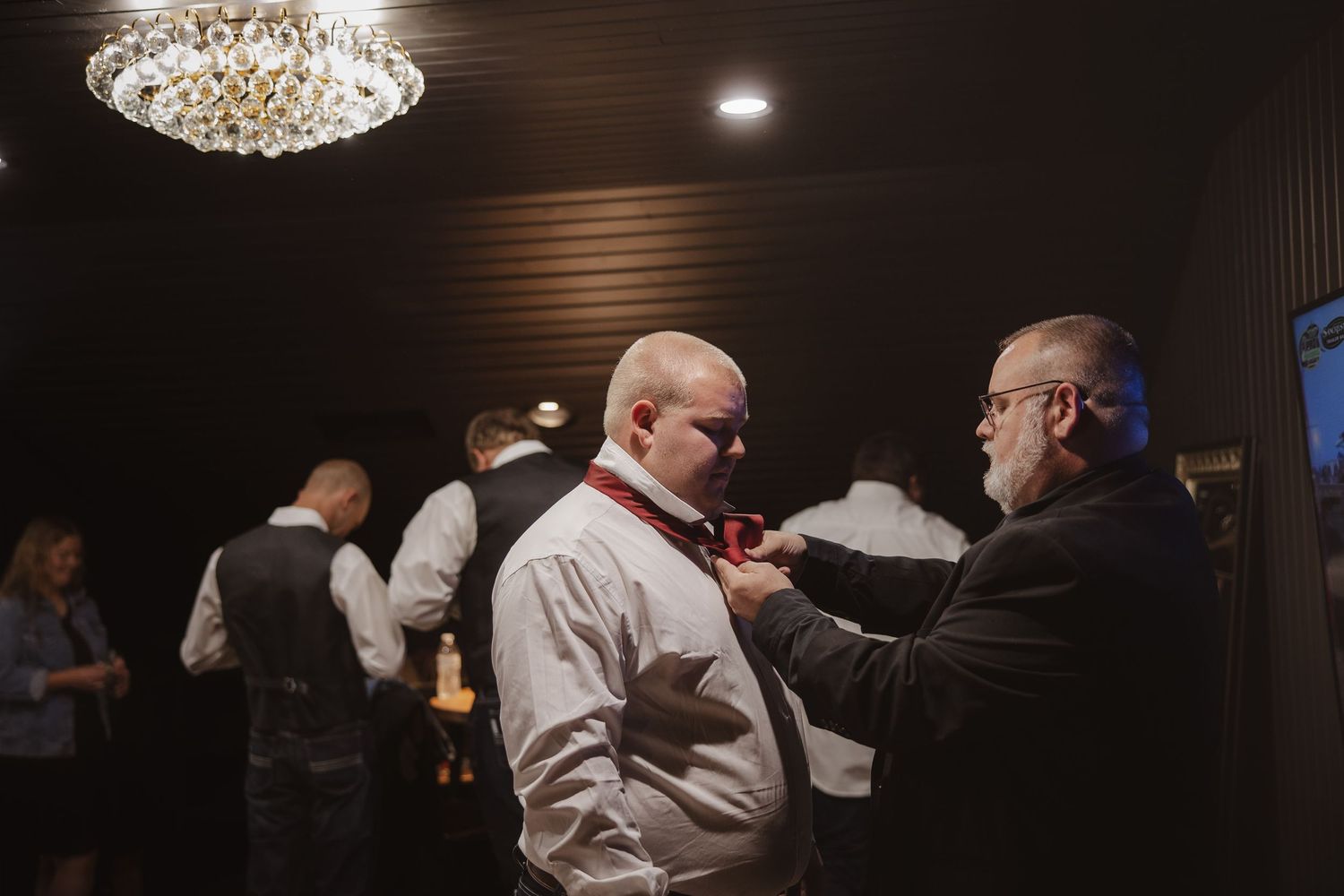Guests dancing and socializing under elegant crystal chandeliers at an evening event in a dark reception hall.