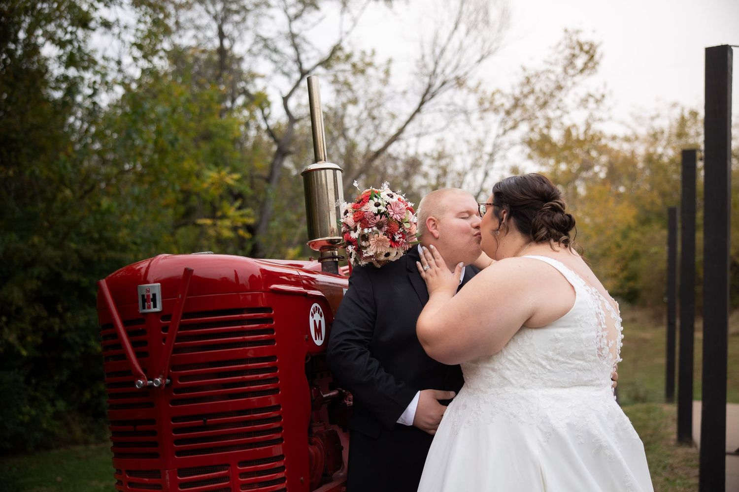 A couple shares a romantic moment in an outdoor setting with a vintage red tractor as their backdrop.