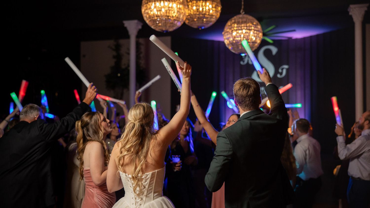 Wedding reception dance floor with guests holding colorful glow sticks under sparkling disco ball lights.