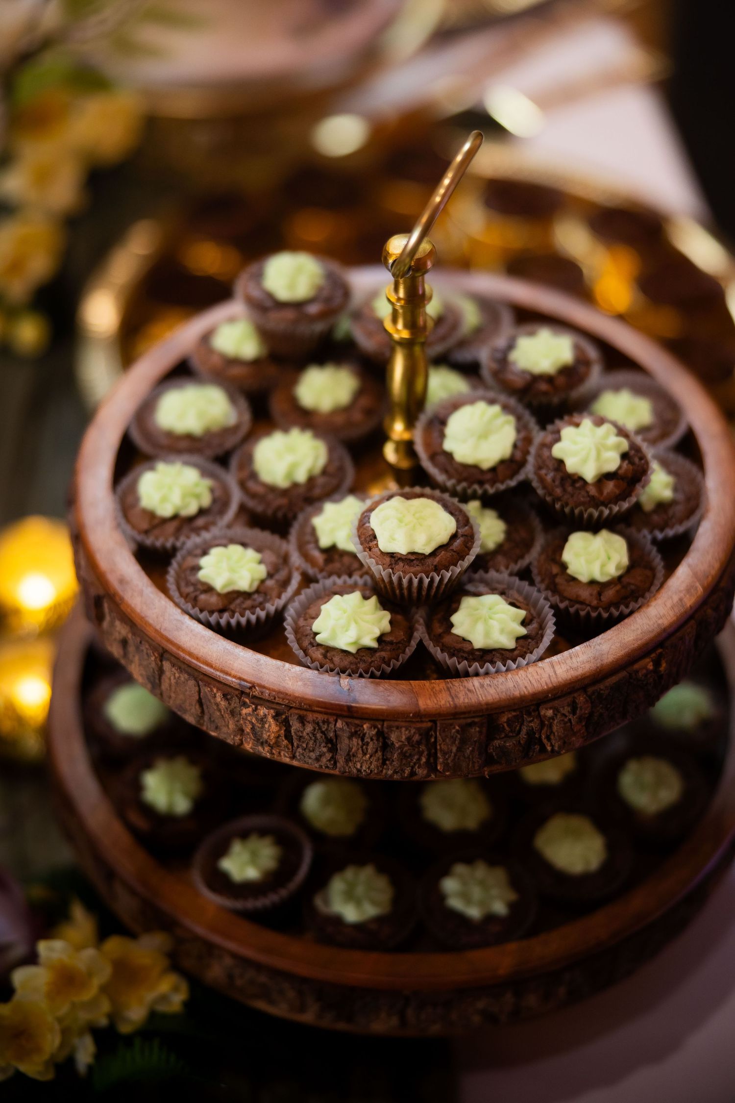 Two-tier rustic wooden dessert stand displaying chocolate cupcakes with green frosting at a wedding reception.